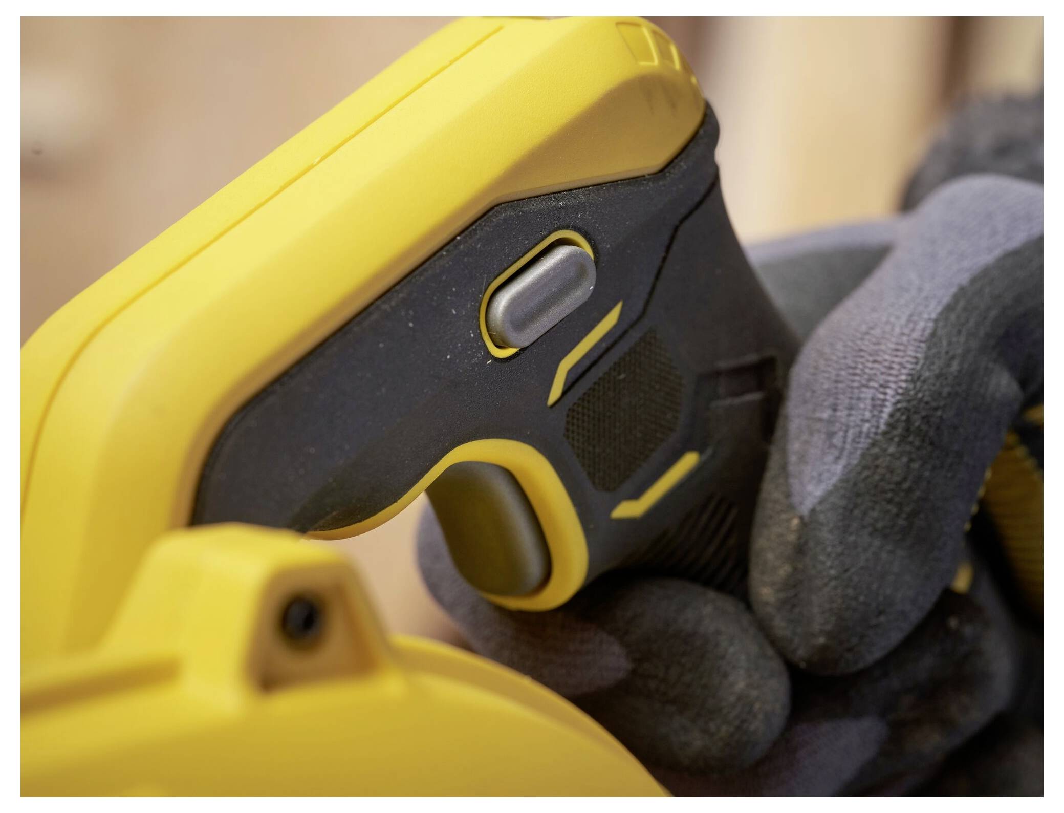 Eine Nahaufnahme der behandschuhten Hand einer Person, die ein gelb-schwarzes Elektrowerkzeug hält, wobei der Fokus auf dem Griff und dem Auslöser liegt.