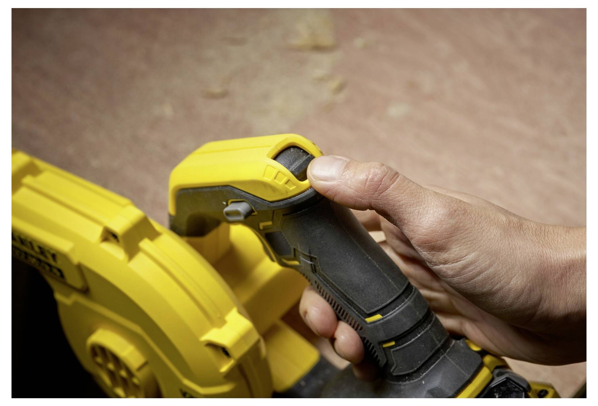 Eine Person greift einen gelben Elektrowerkzeuggriff mit schwarzem Griff und bereitet sich darauf vor, ihn auf einem Holzflächenhintergrund zu bedienen.