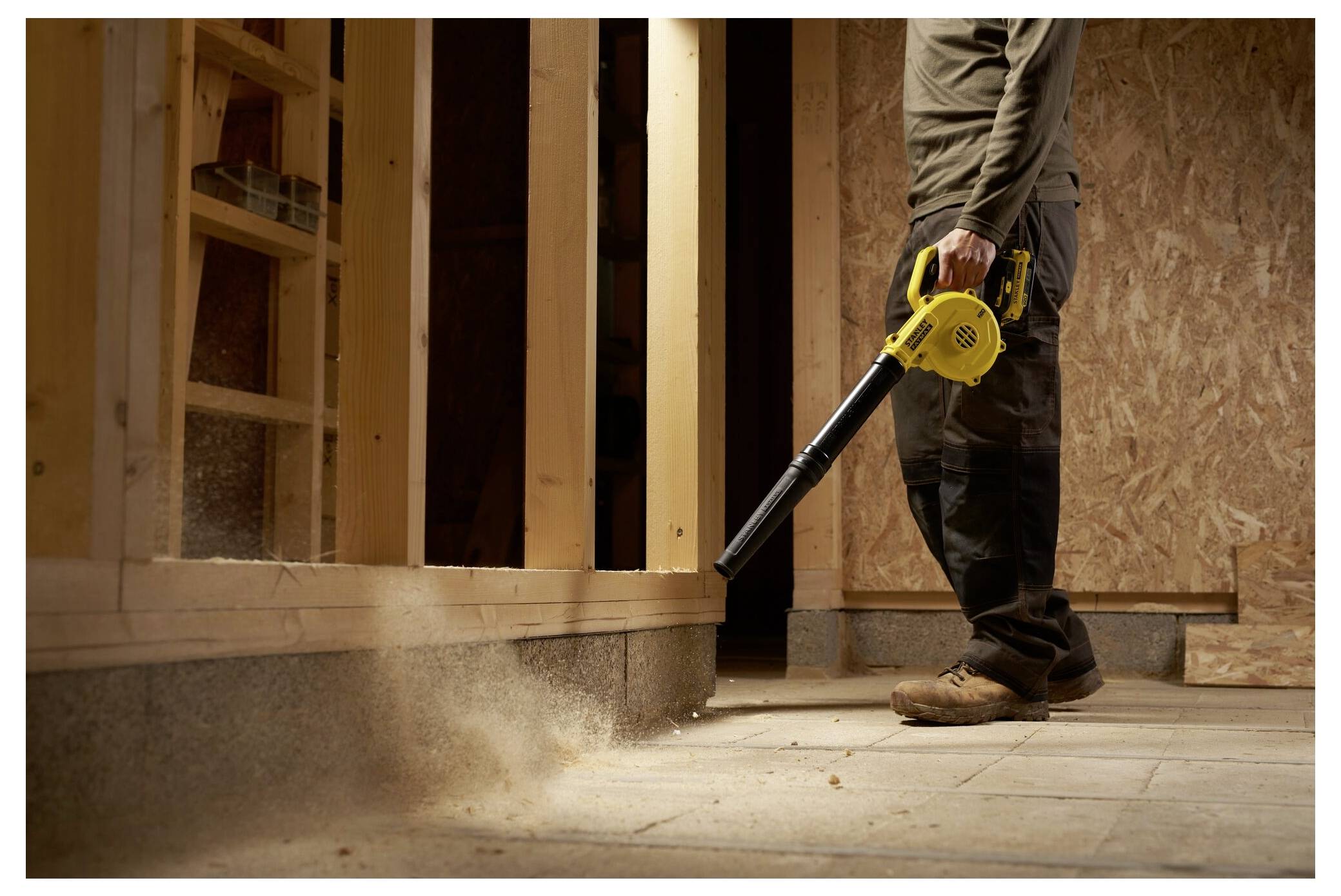 Ein schwarzer und gelber Rasentrimmer schneidet durch überwuchertes Gras in einem Garten, mit Bäumen im Hintergrund.