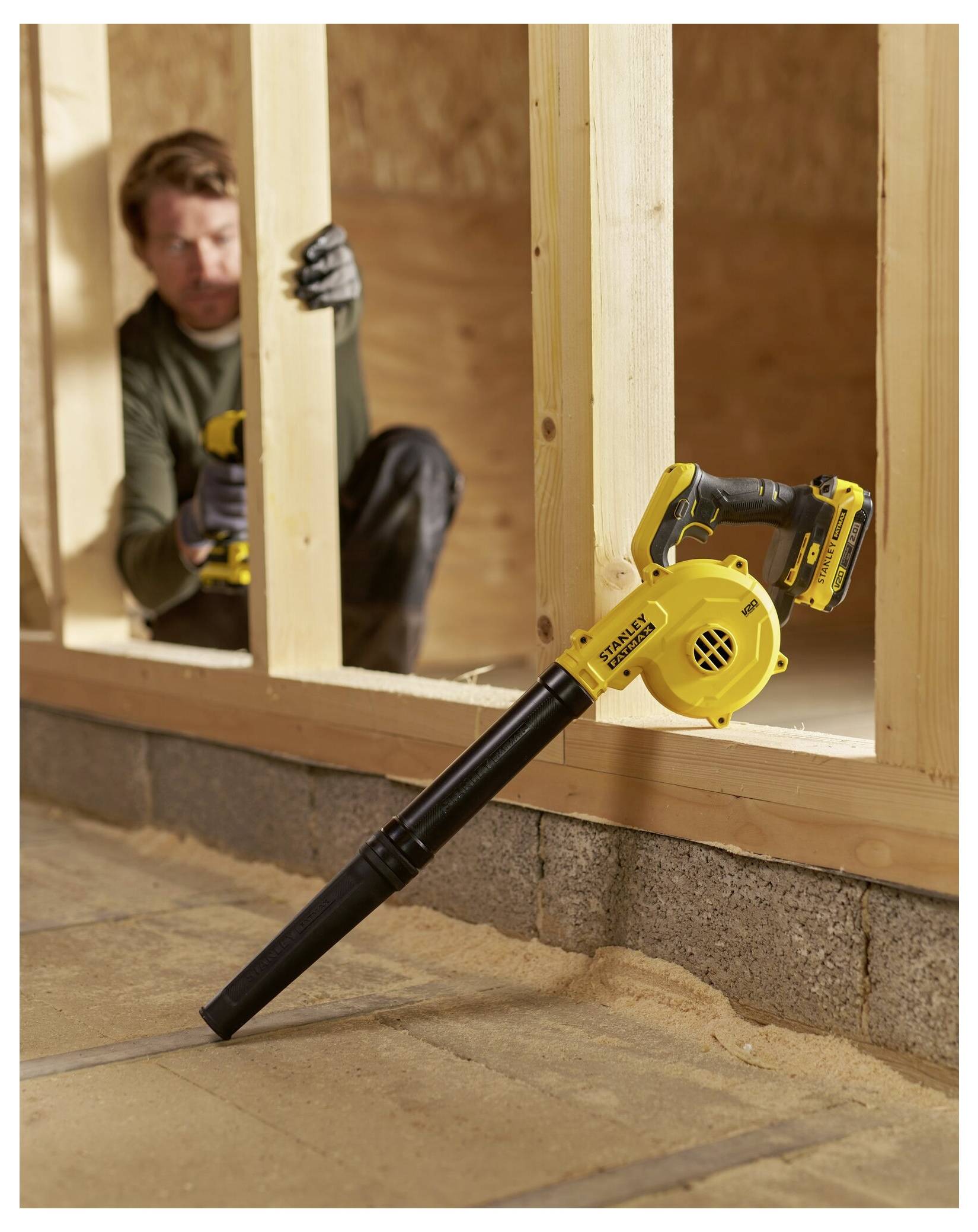 Eine Person verwendet ein gelbes Stanley-Elektrowerkzeug mit einer Schleifband-Aufsatz, um die Innenseite eines quadratischen Metallrohrs auf einem Holztisch zu schleifen.