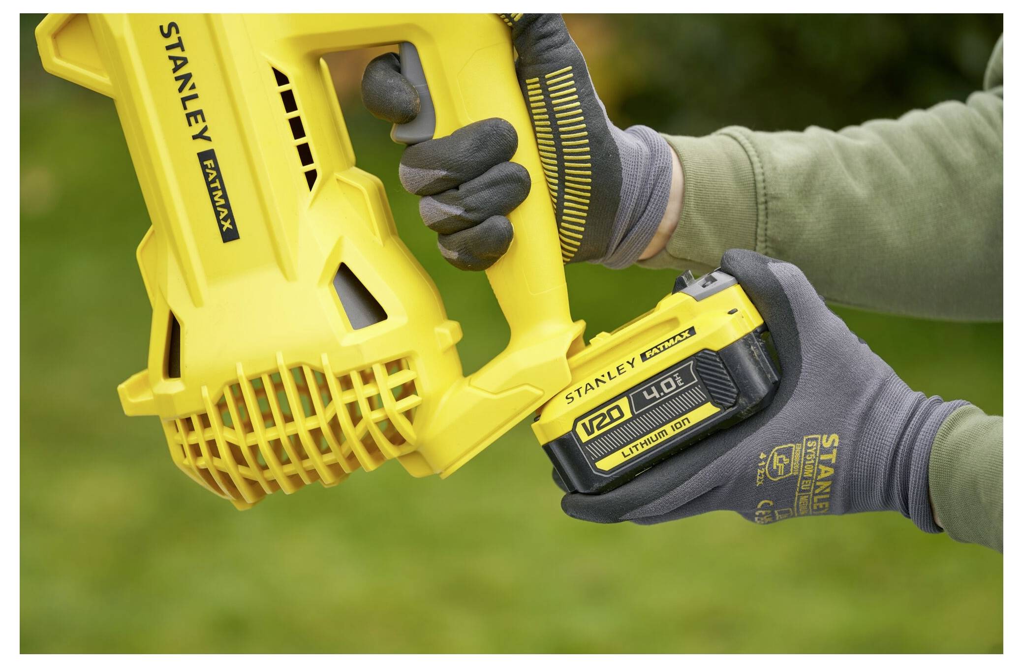 Eine behandschuhte Hand verstellt ein schwarzes Kabel an einem gelben Stanley Fatmax V20-Ladegerät. Der Fokus liegt auf der Verbindungsstelle des Geräts.