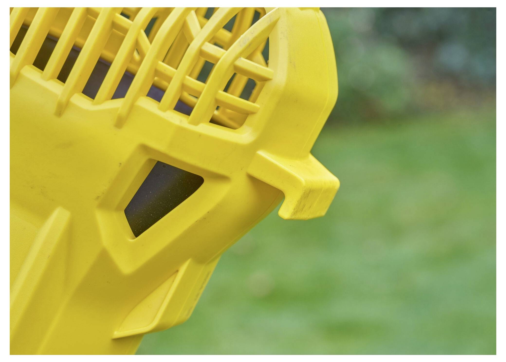 Nahaufnahme eines gelben Kunststoffgeräts mit gitterartigen Strukturen, vor einem unscharfen grünen Hintergrund.
