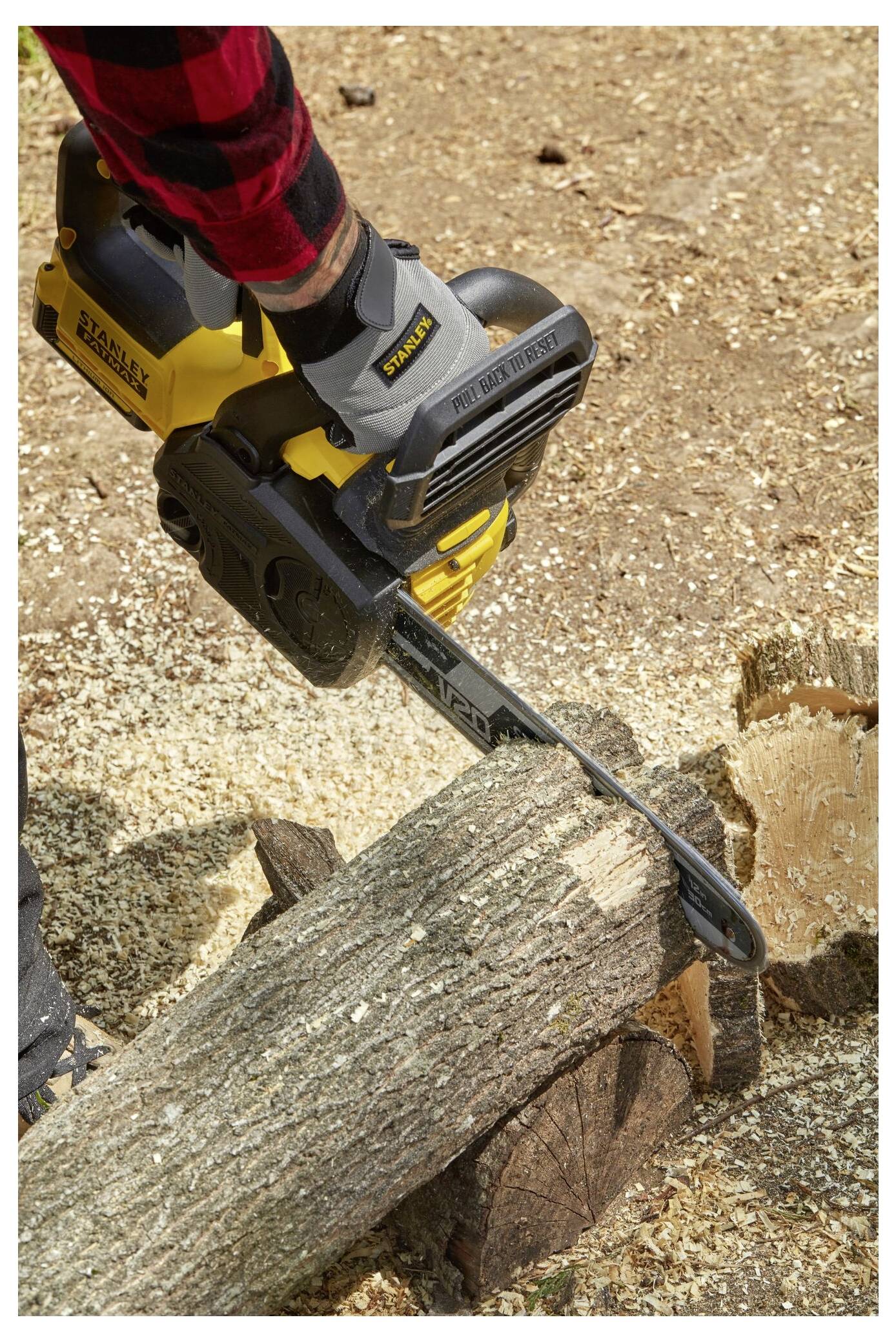 Eine Person in einem roten karierten Hemd benutzt eine gelbe kabellose Kettensäge, um einen Baumstamm zu schneiden, umgeben von Holzspänen auf dem Boden.