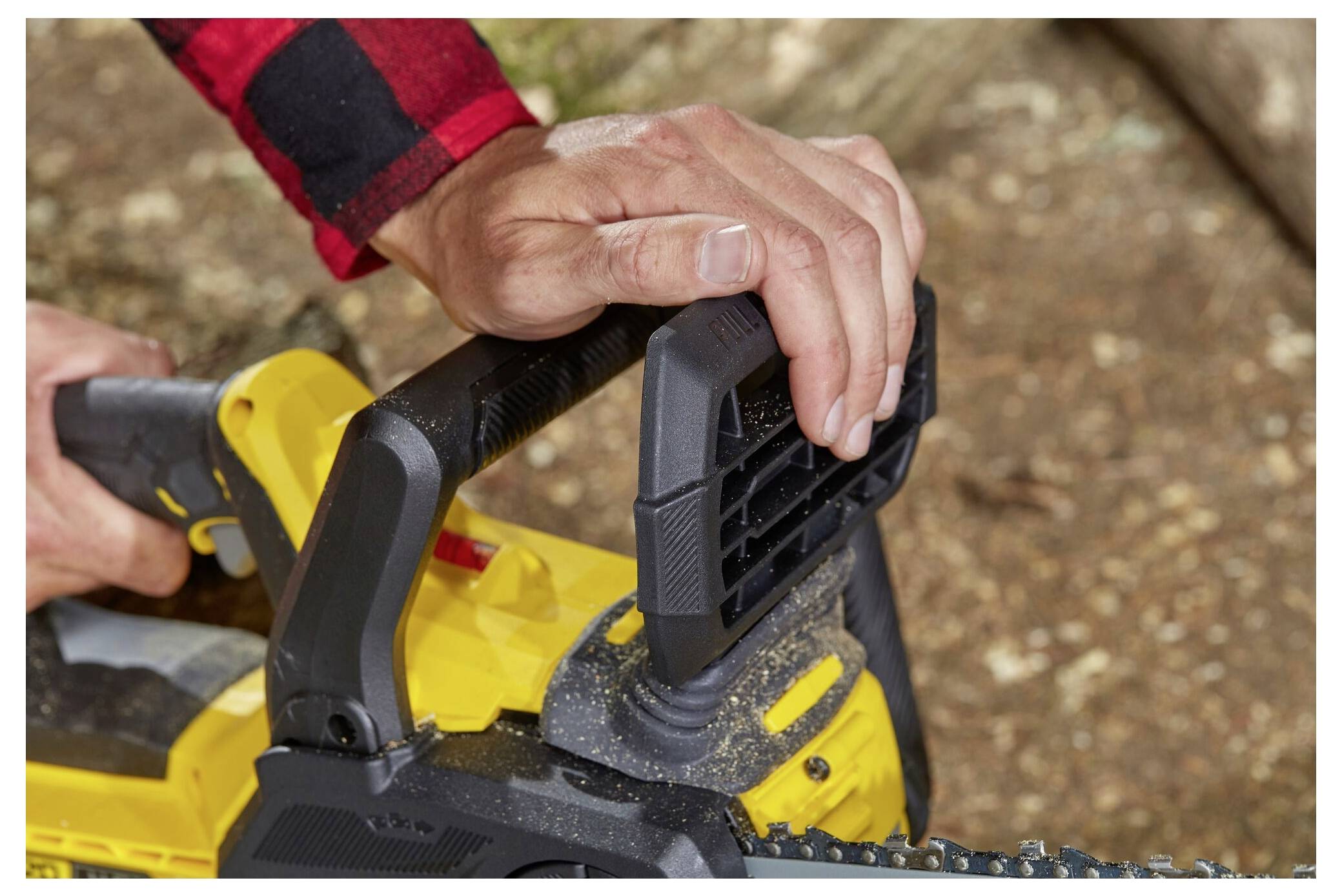 Eine Person, die eine gelbe Kettensäge im Freien bedient, den Griff fest mit beiden Händen erfasst, was Sicherheit und Kontrolle zeigt.