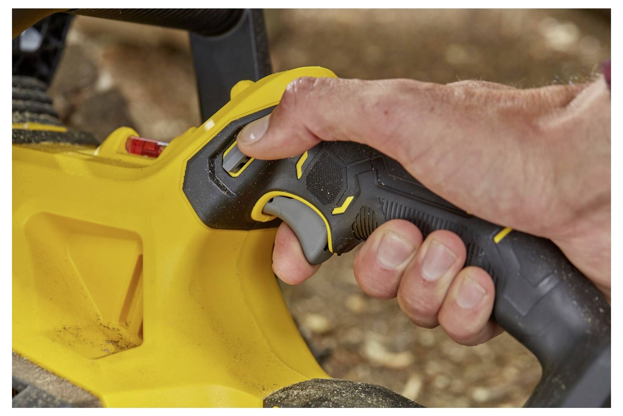 Eine Person greift einen schwarz-gelben Griff eines Elektrowerkzeugs und drückt einen Knopf, möglicherweise um das Werkzeug zu steuern. Der Hintergrund ist verschwommen.