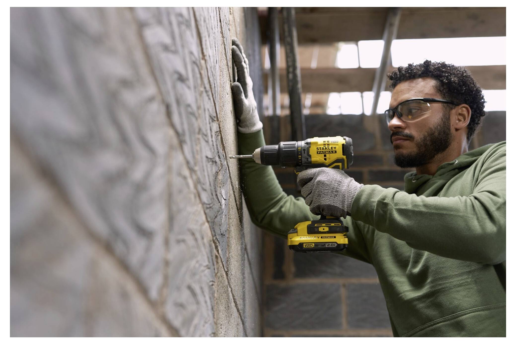 Eine Person mit grauen Handschuhen hält einen gelben und schwarzen Akku-Bohrschrauber mit der Aufschrift 