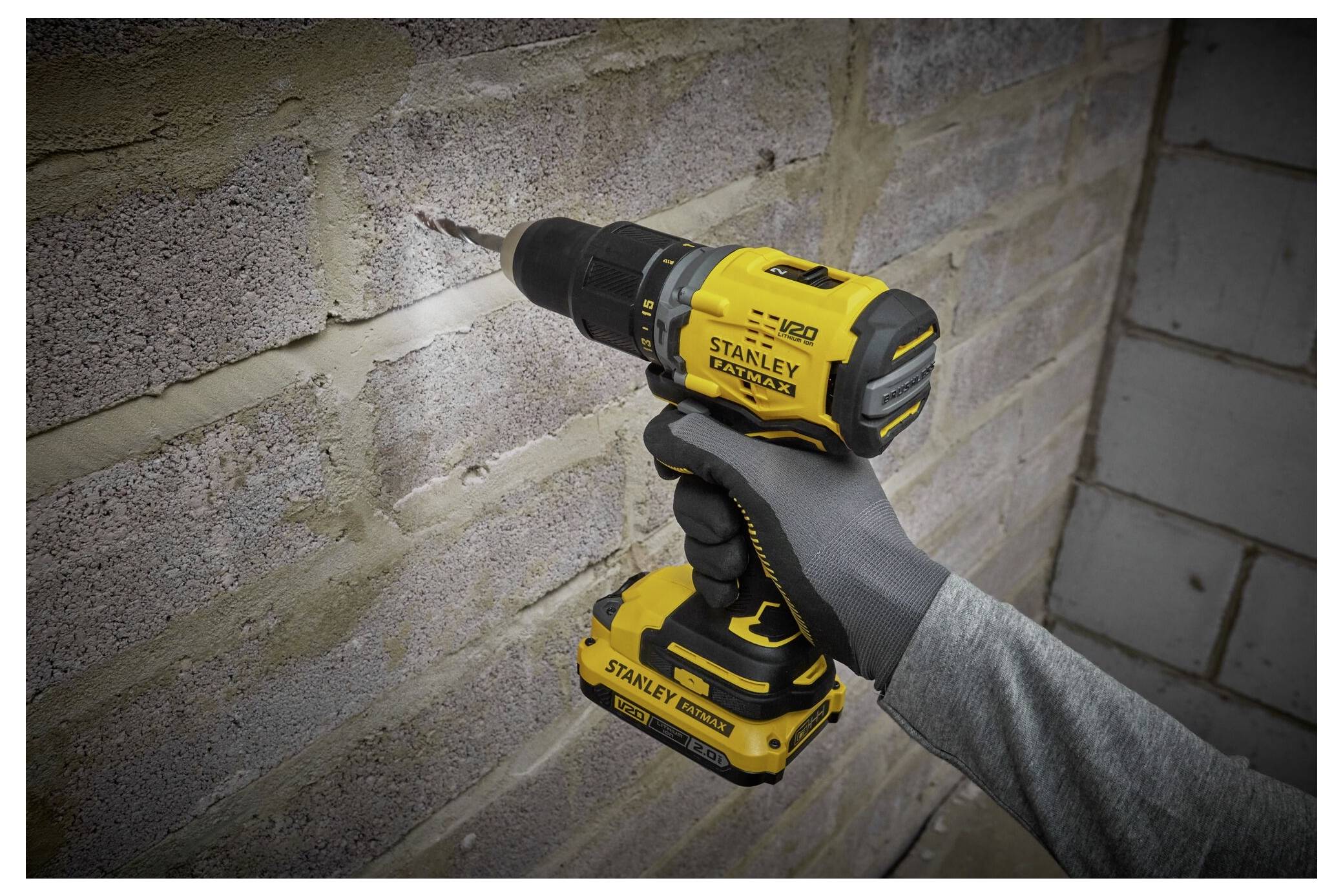 Eine Person, die einen gelben kabellosen Elektrobohrer verwendet, um ein Loch in eine Backsteinmauer zu bohren, trägt dabei einen grauen Schutzhandschuh.