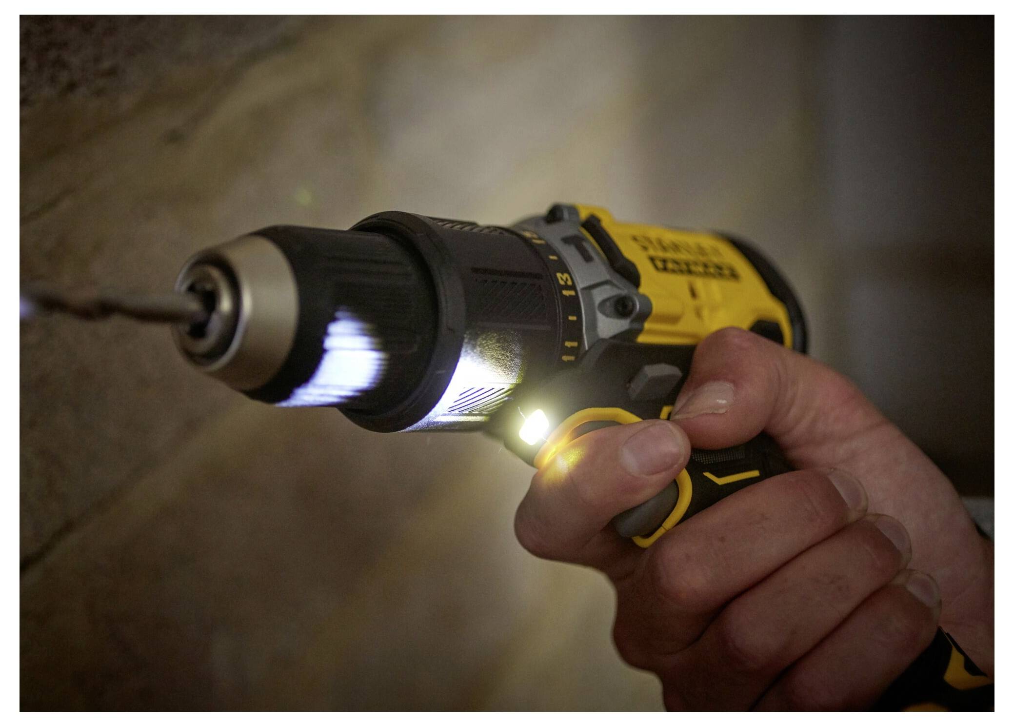 Eine Person mit Schutzbrille verwendet einen gelben kabellosen Bohrer, um ein Loch in einen Holzbalken in einer Baustelle zu bohren.