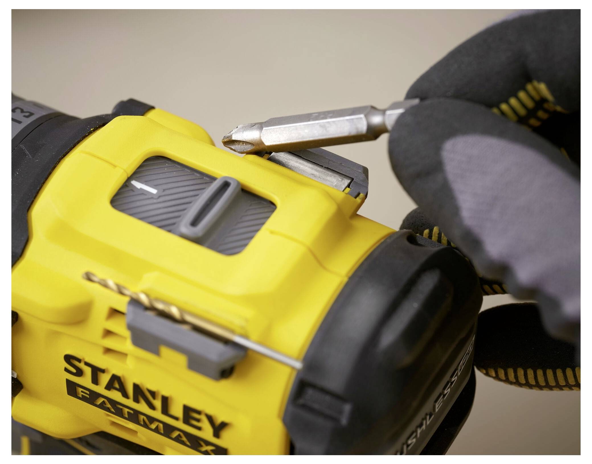 Nahaufnahme einer Person, die Handschuhe trägt und einen Bohraufsatz in ein gelbes Stanley Fatmax Elektrowerkzeug einsetzt.