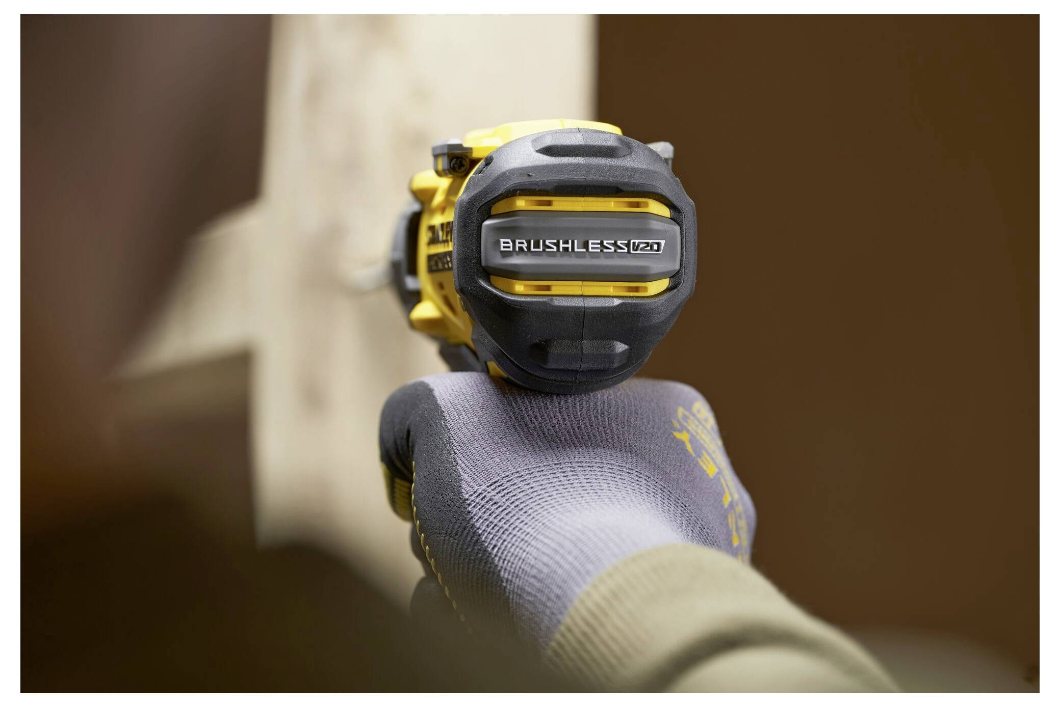 Eine Person, die einen Handschuh trägt, benutzt einen gelben kabellosen Elektroschrauber auf einer hellen Holzoberfläche.