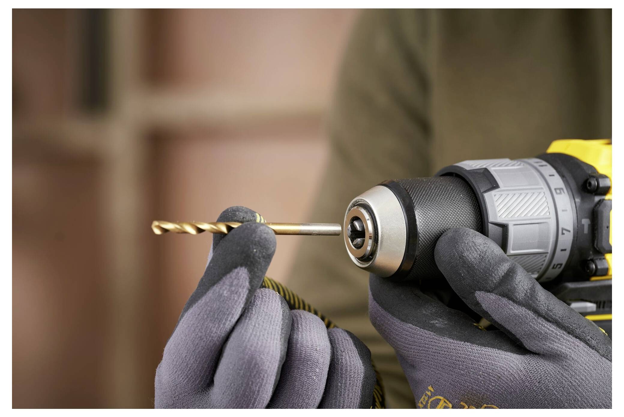 Eine behandschuhte Hand hält einen Bohraufsatz über einem gelben Stanley Fatmax Elektrowerkzeug und ist bereit, ihn zum Gebrauch in das Bohrfutter einzuführen.