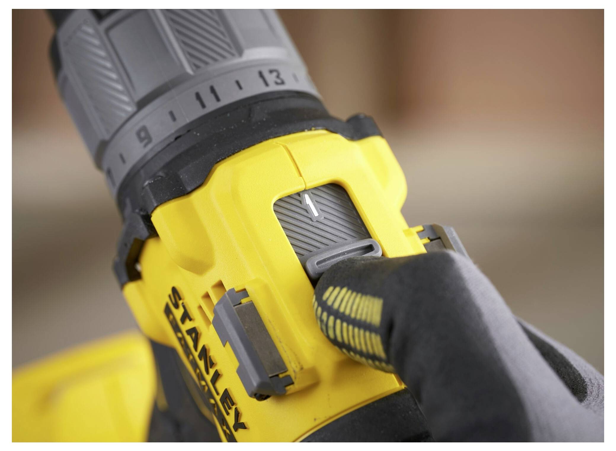 Eine behandschuhte Hand stellt die Drehmomenteinstellung an einem gelb-schwarzen Elektrobohrer ein.