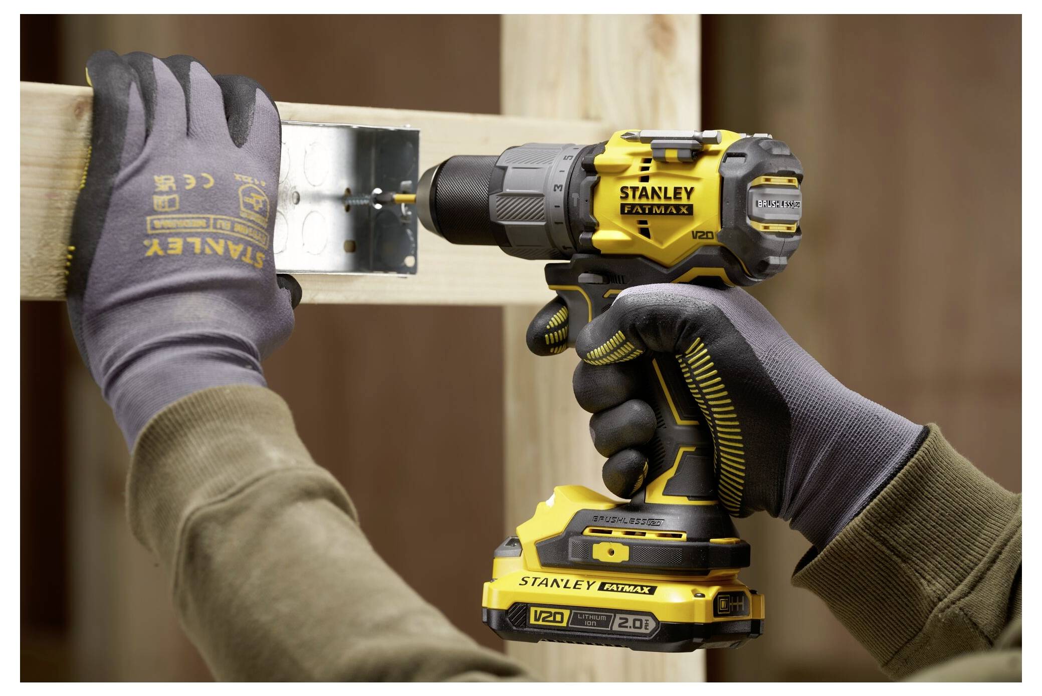 Eine Person verwendet einen Stanley Fatmax Bohrer, um eine Metallhalterung mit einer Holzstütze zu verschrauben, während sie zum Schutz Schutzhandschuhe trägt.