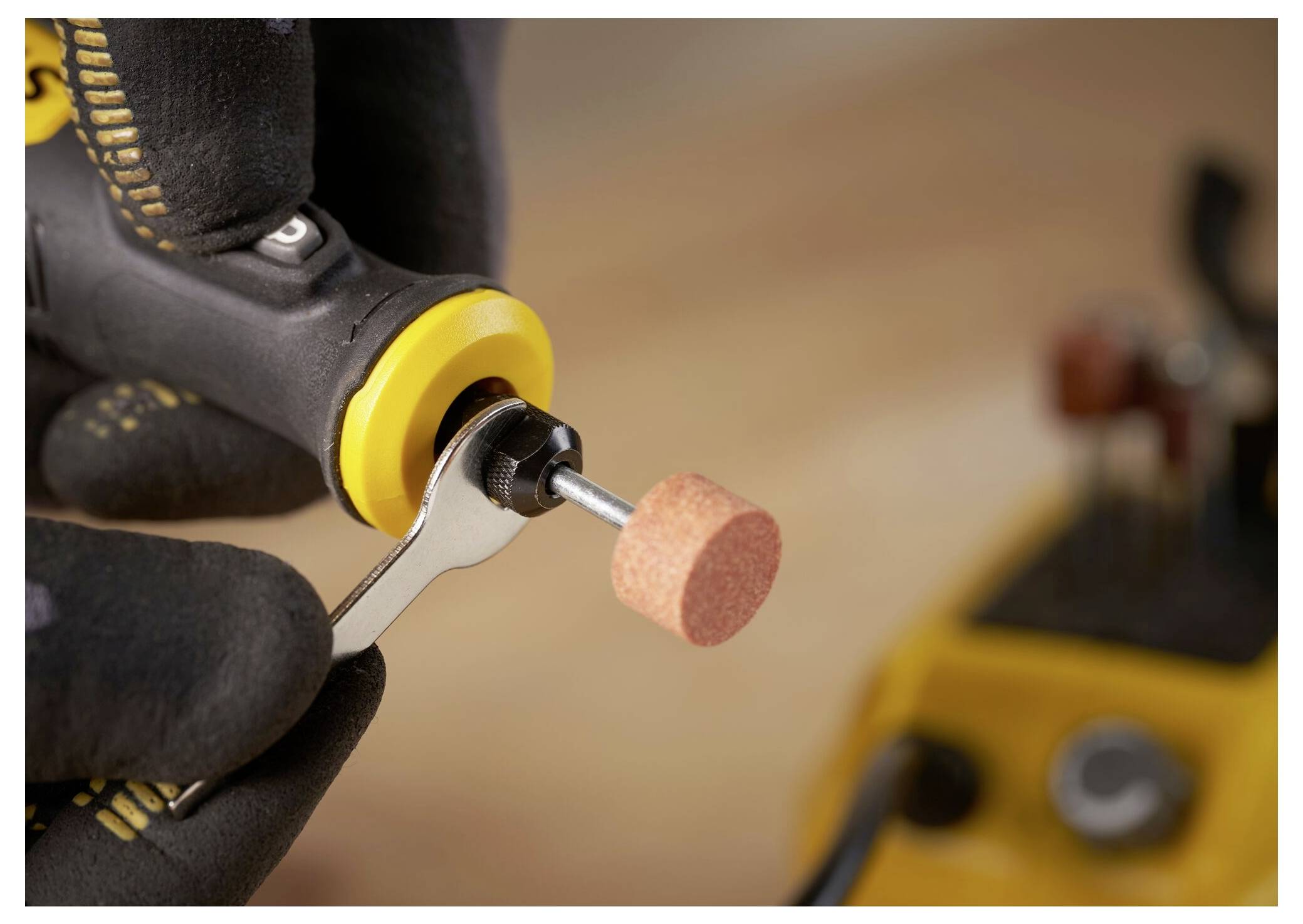 Eine Person benutzt eine gelbe Elektrobohrmaschine mit einem Schneckenbohrer, um in den grasbewachsenen Boden zu bohren. Holzpfähle liegen in der Nähe.