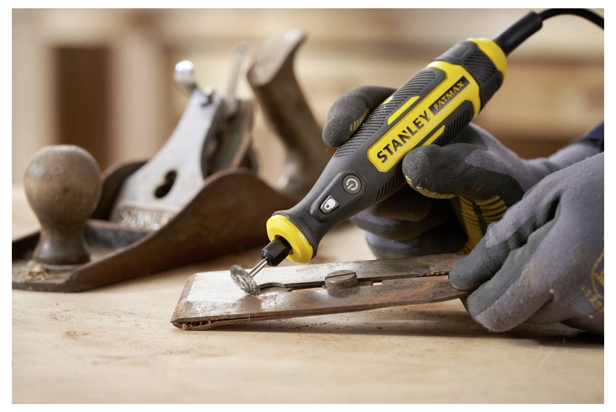 Eine Person in Schutzausrüstung schneidet mit einer Kettensäge Holz im Freien in der Nähe einer Steinmauer. Im Hintergrund sind gefallene Äste und ein Weg sichtbar.