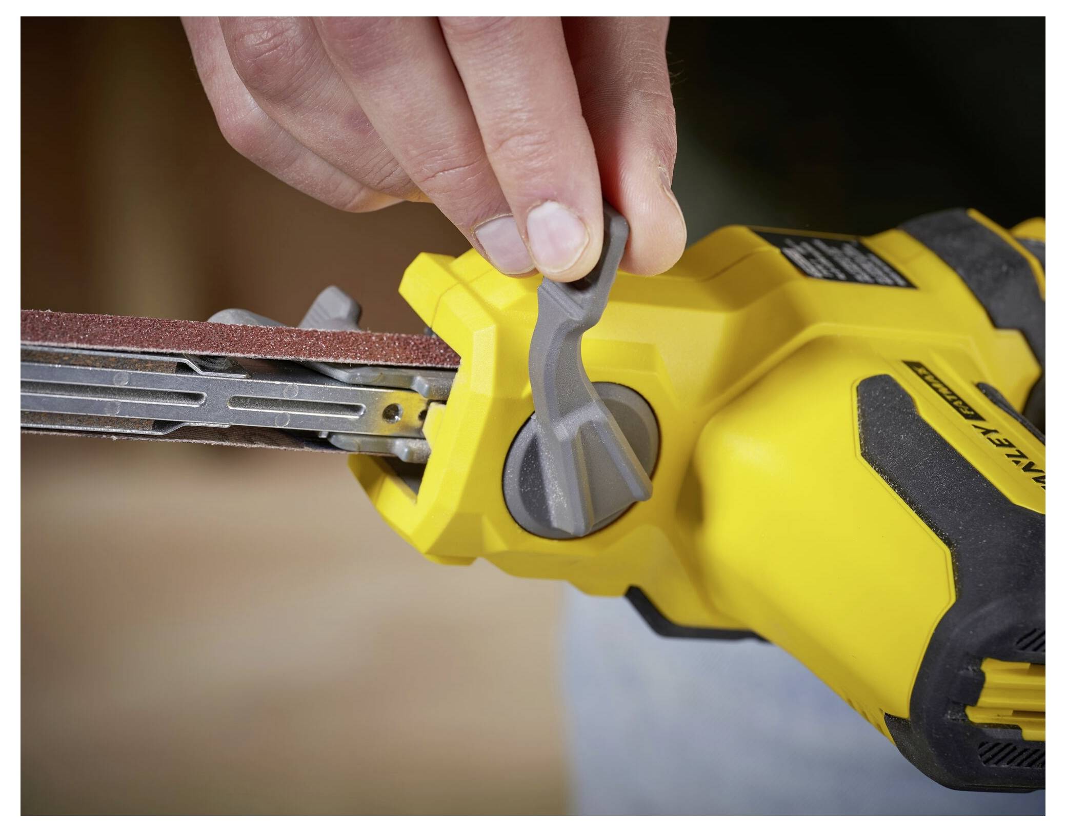 Eine Person stellt den Hebel eines gelben Bandschleifers ein und zeigt damit die Wartung oder Funktionalität des Werkzeugs.