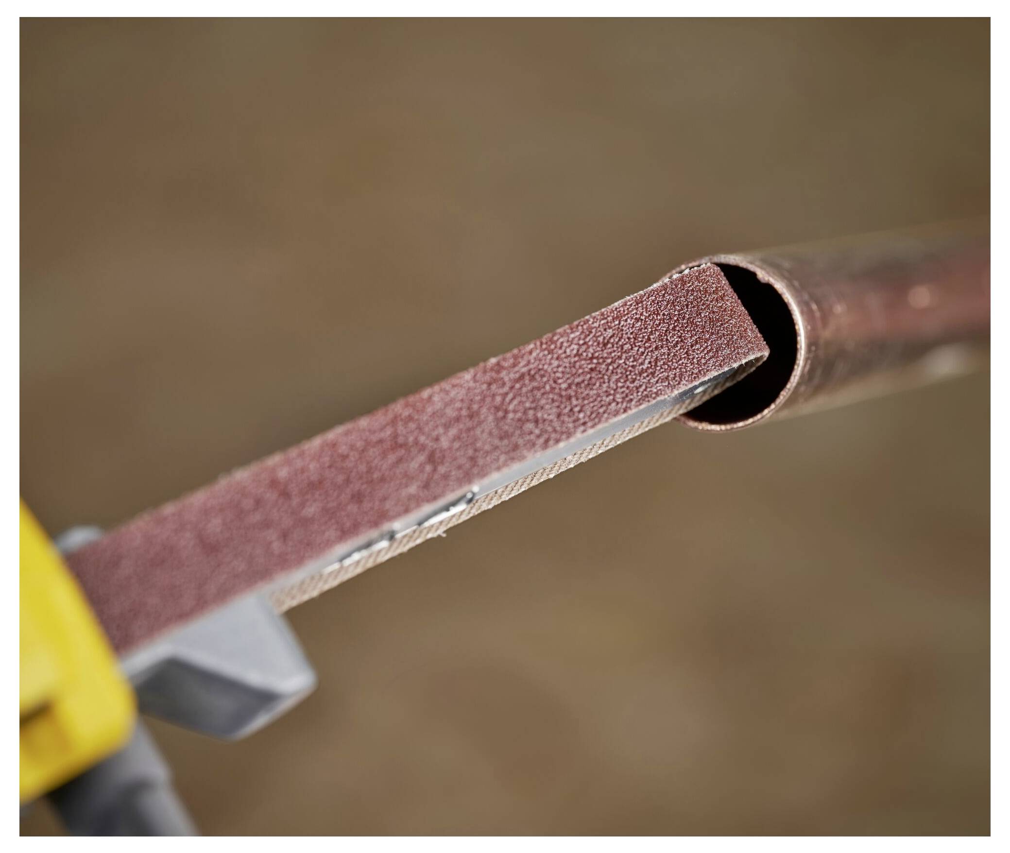 Eine Nahaufnahme zeigt ein Schleifwerkzeug, das die Kante eines Kupferrohrs glättet und auf eine Bau- oder Klempneraufgabe hindeutet.