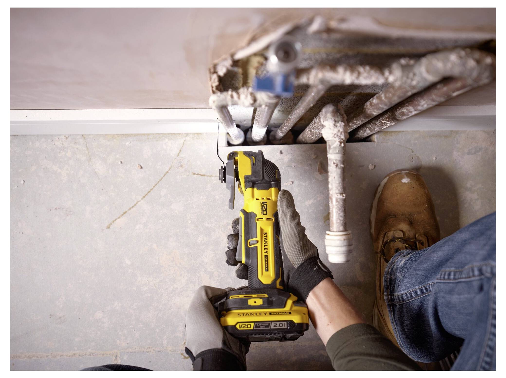 Eine Person, die ein gelbes Elektrowerkzeug zum Schneiden von Rohren in der Nähe einer Wand verwendet, trägt Handschuhe und Arbeitsschuhe und führt möglicherweise Wartungs- oder Reparaturarbeiten durch.