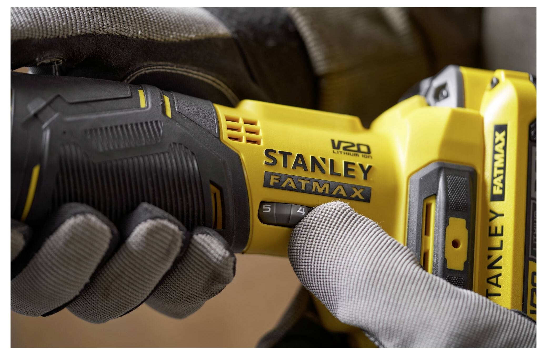 Eine behandschuhte Hand greift ein Stanley Fatmax V20 Elektrowerkzeug und zeigt die Geschwindigkeitseinstellungen und das ergonomische Design.