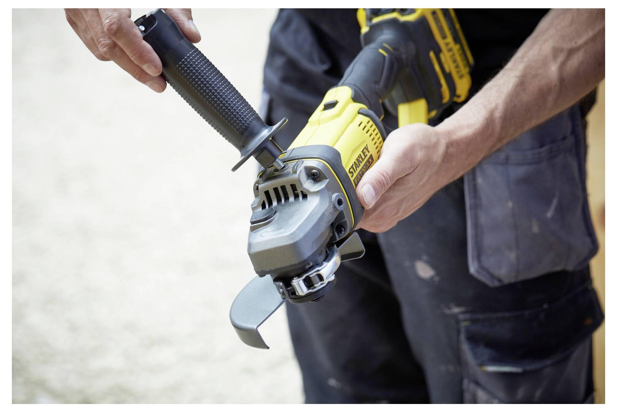 Eine Person hält einen gelb-schwarzen Winkelschleifers und positioniert den Griff mit beiden Händen. Das Werkzeug wirkt neu und ungenutzt.