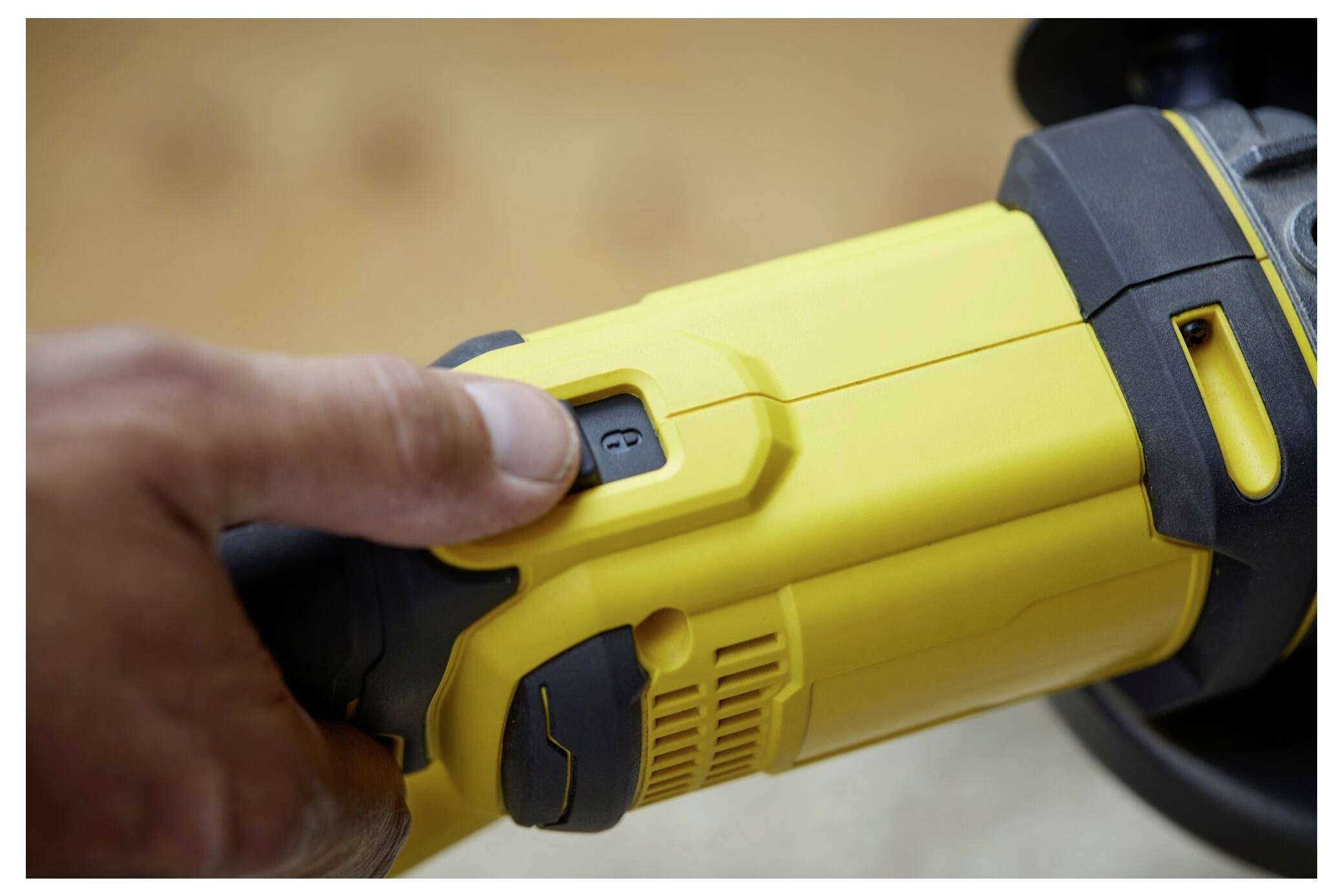 Eine Person schaltet ein gelbes Elektrowerkzeug ein, indem sie seinen schwarzen Auslöseschalter drückt, wodurch seine Funktionsweise und Designmerkmale hervorgehoben werden.