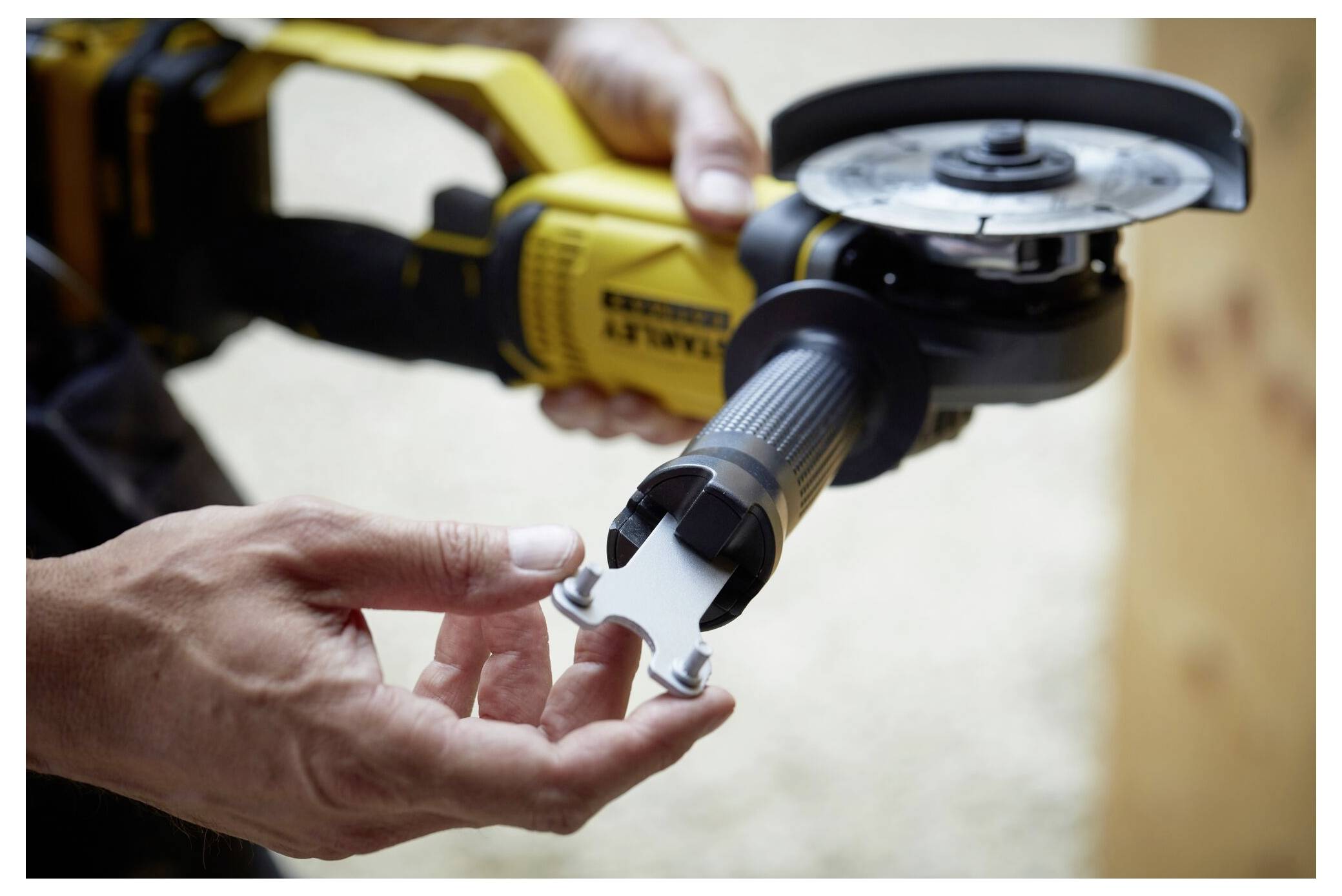 Eine Person, die einen gelb-schwarzen Winkelschleifer hält, setzt einen Schraubenschlüssel auf die Scheibe zur Justierung an. Der Fokus liegt auf Händen und Werkzeug.