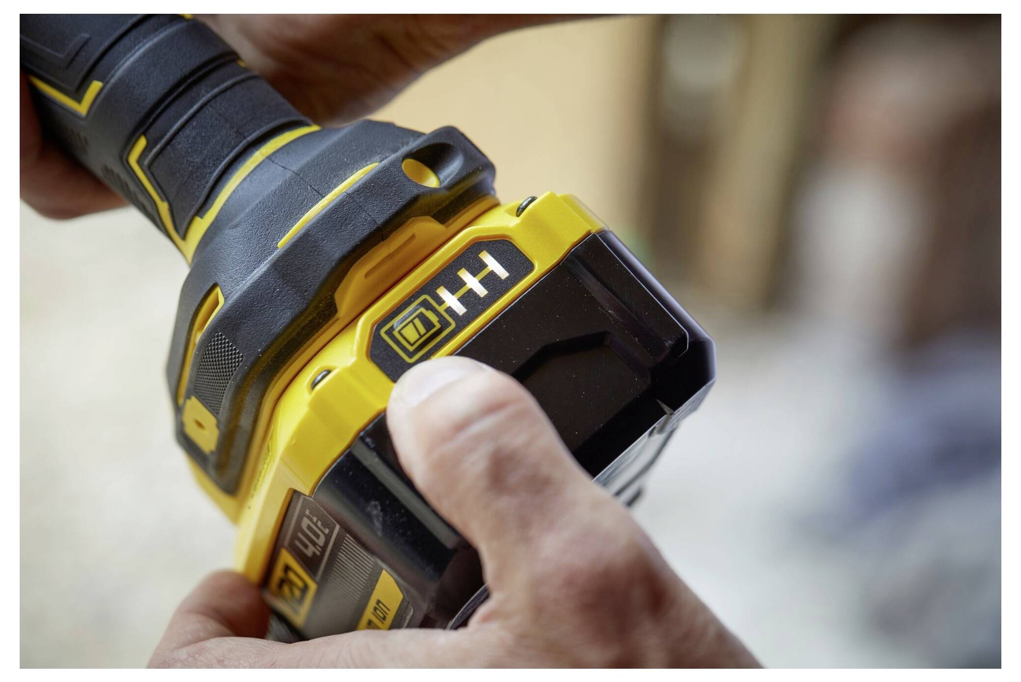 Eine Person hält ein gelb-schwarzes kabelloses Elektrowerkzeug und konzentriert sich auf den Batteriebereich, wobei eine Hand einen Knopf mit der Beschriftung 