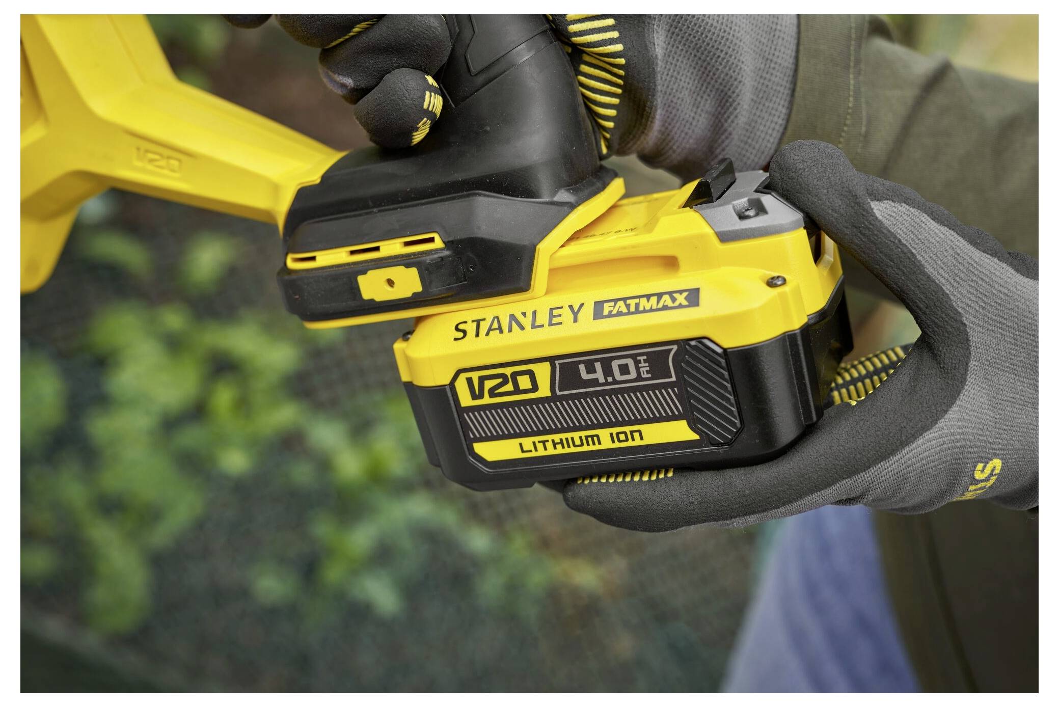 Eine Person, die Handschuhe trägt, setzt einen STANLEY FATMAX 4.0 Ah Lithium-Ionen-Akku in ein gelbes Elektrowerkzeug im Freien ein.