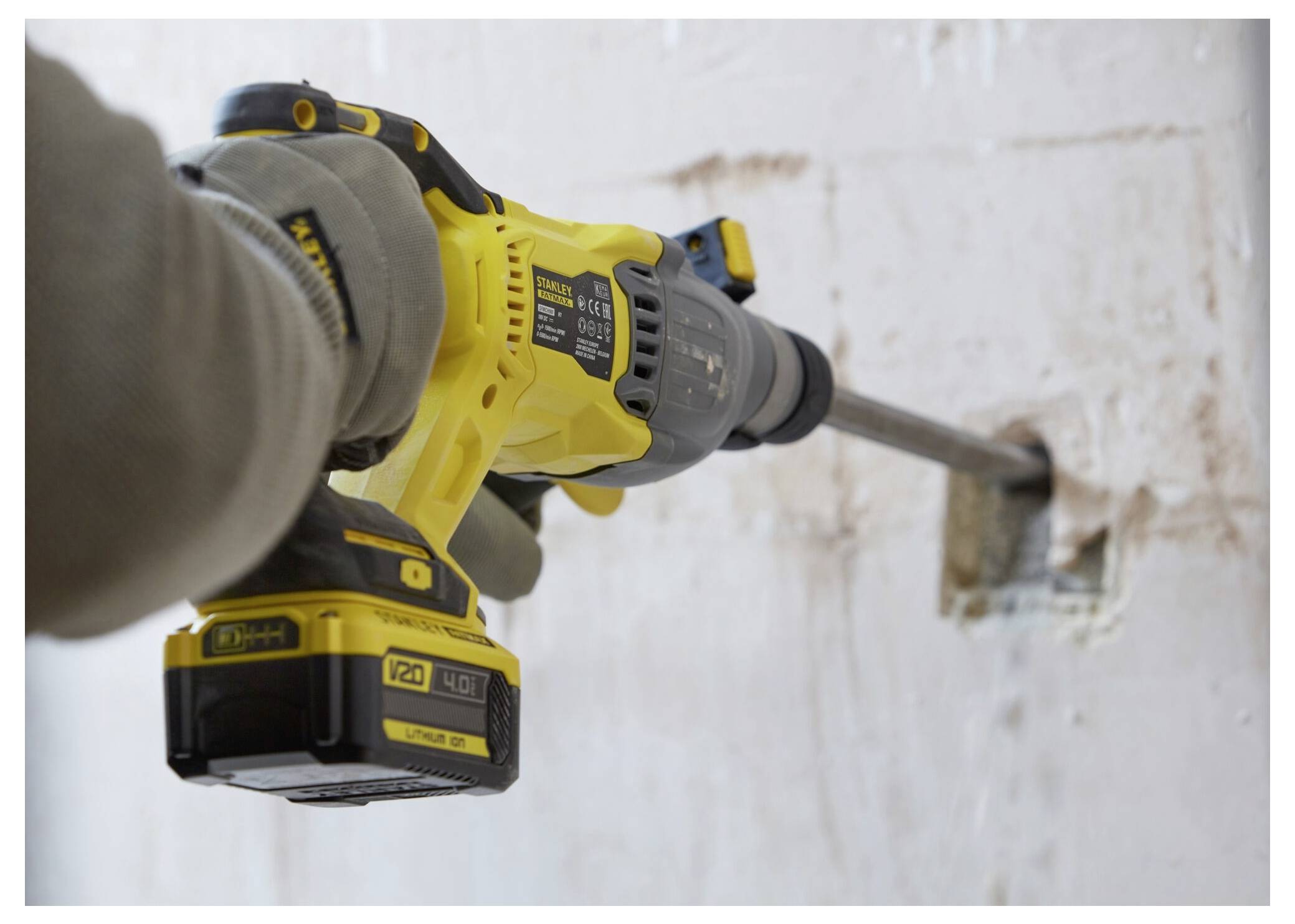 Eine Person benutzt eine gelbe kabellose Bohrmaschine mit einem großen Bohrer, um ein Loch in eine weiße Wand zu bohren, während sie zum Schutz Handschuhe trägt.