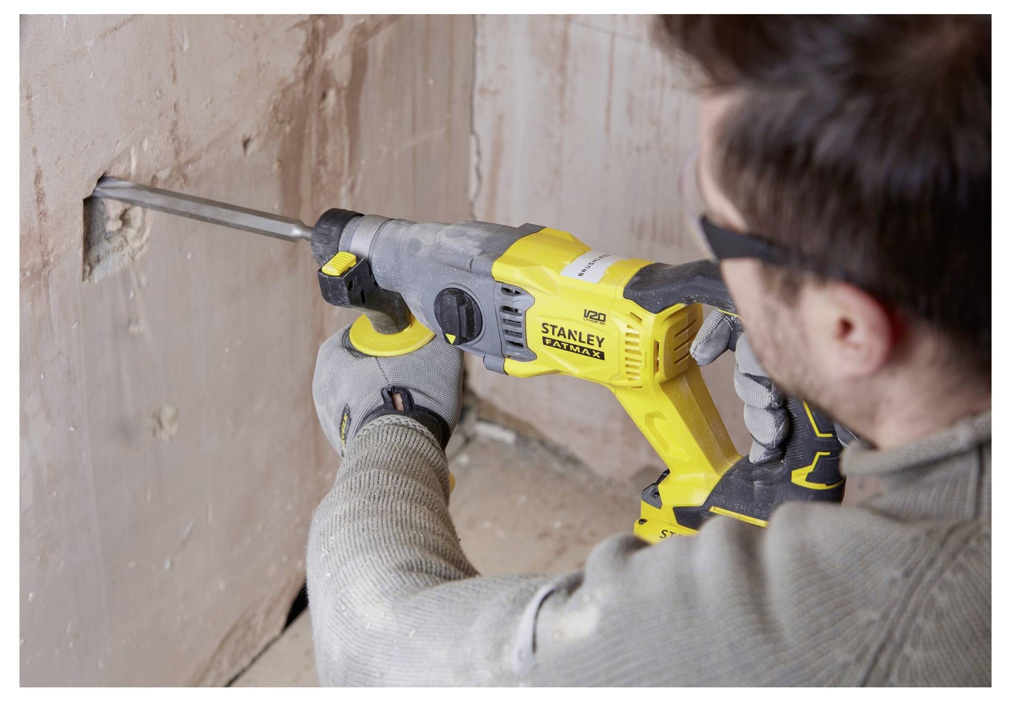 Eine Person, die einen gelb-schwarzen Elektro-Bohrhammer verwendet, um Putz von einer Wand abzuschlagen, trägt dabei Schutzhandschuhe und eine Schutzbrille.