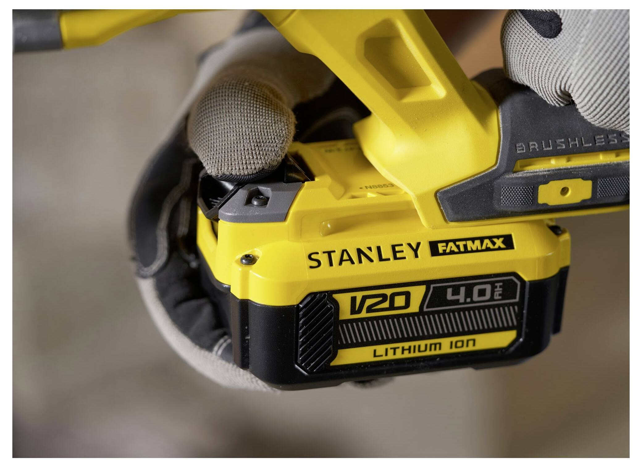 Eine Person in Handschuhen hält eine gelbe Stanley Fatmax V20 4.0Ah Lithium-Ionen-Batterie und zeigt die Marke und Kapazität.