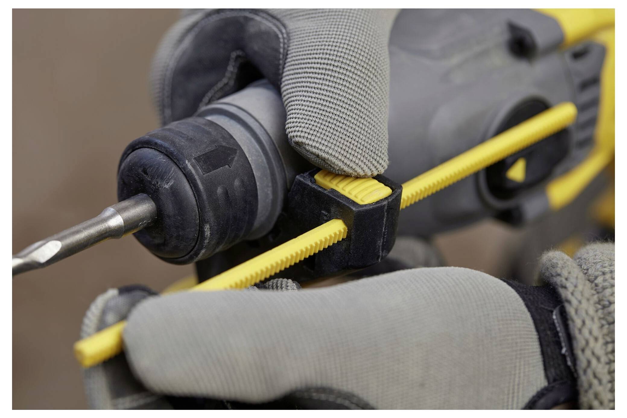 Eine Person mit grauen Handschuhen stellt ein gelbes Werkzeug ein, das an einem Bohrer befestigt ist, wobei der Fokus auf der Vorbereitung für präzise Arbeit liegt.