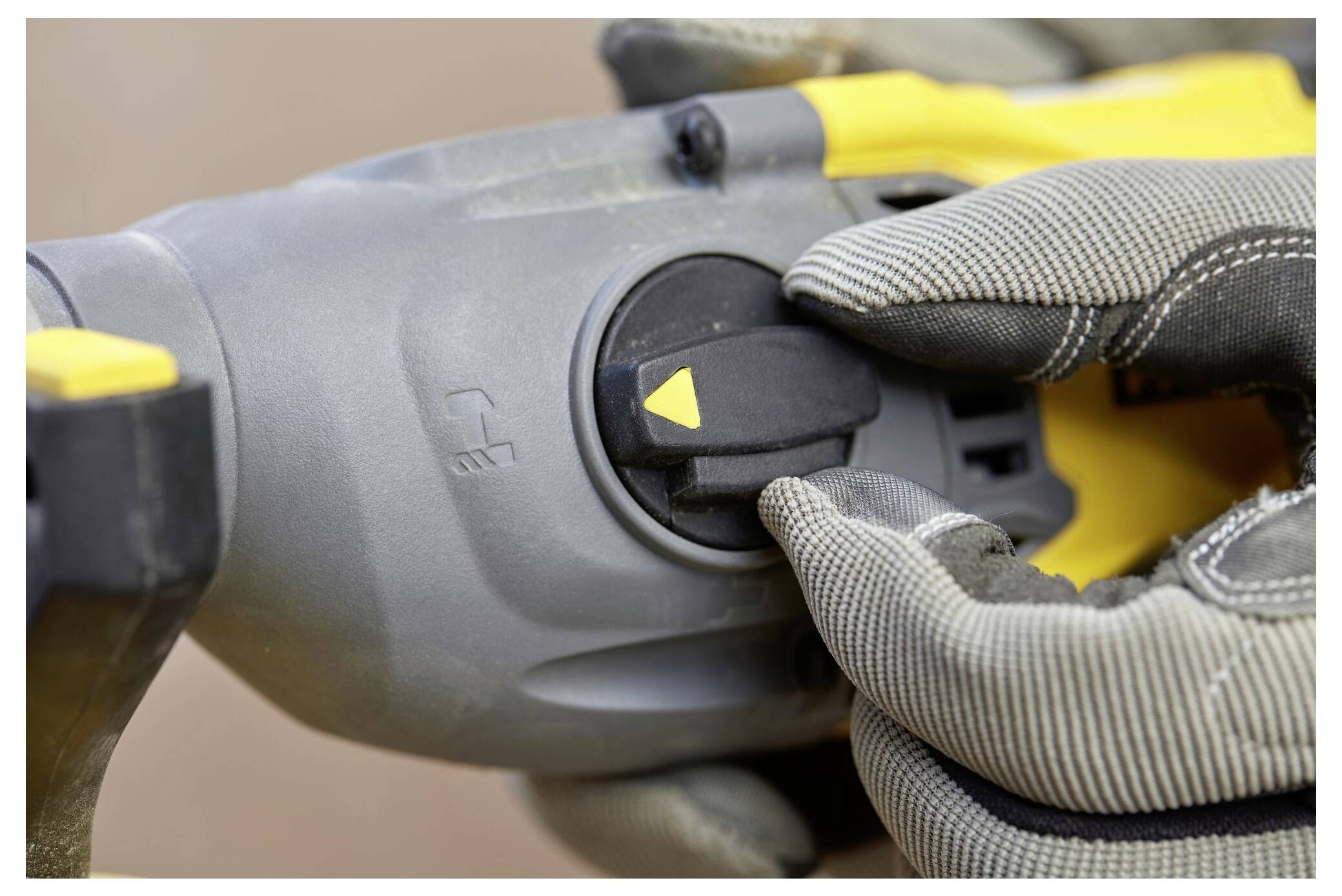 Eine behandschuhte Hand stellt die Einstellung an einem Elektrowerkzeug ein und konzentriert sich auf ein kreisförmiges Zifferblatt mit einem gelben Dreieck-Indikator.