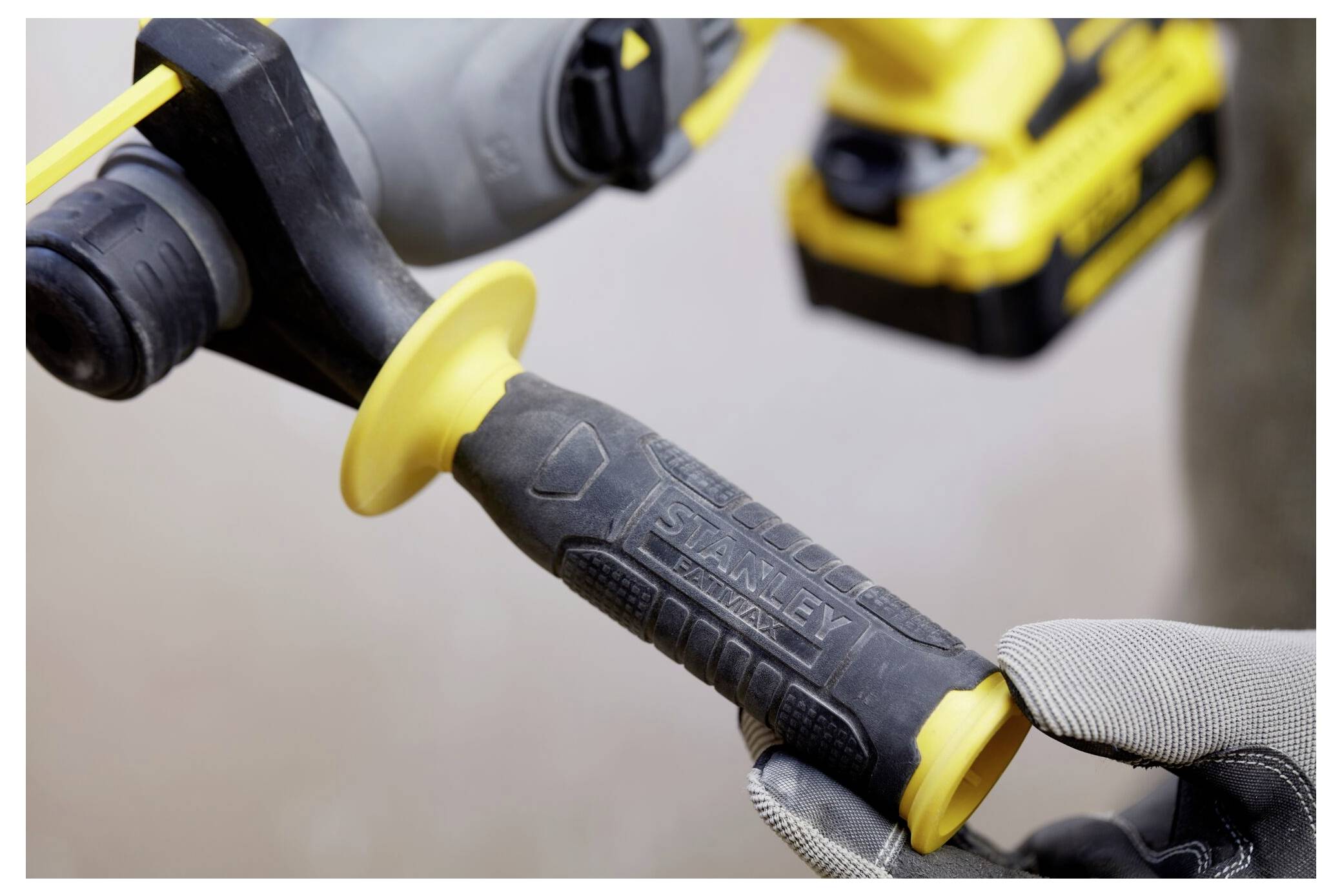 Eine Großaufnahme einer behandschuhten Hand, die den Griff eines Elektrowerkzeugs hält. Das Werkzeug hat einen schwarzen Gummigriff mit dem eingepressten Markennamen.