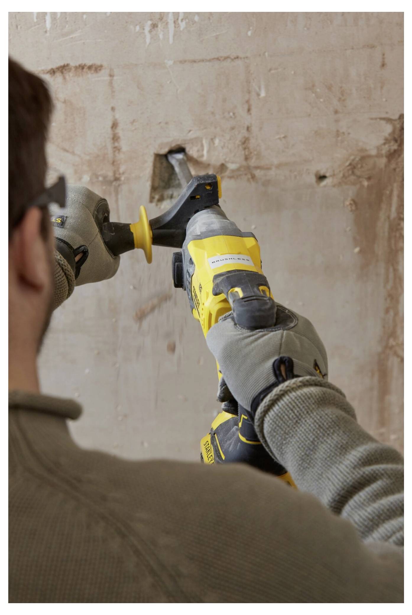 Eine Person mit Handschuhen benutzt ein gelbes Elektrowerkzeug, um eine Wand zu schleifen und deren Oberfläche zu glätten.