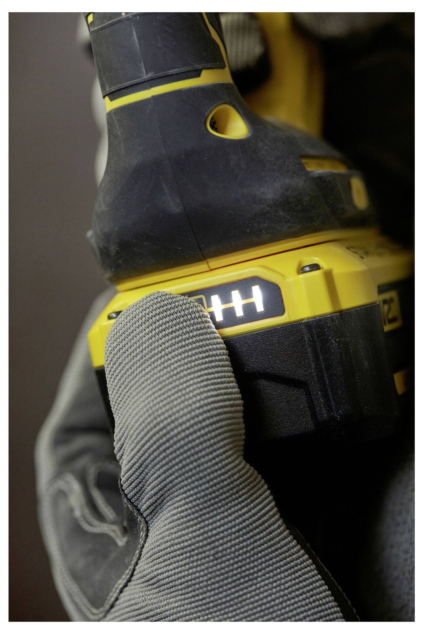 Eine behandschuhte Hand hält einen gelben Elektroschrauber, der eine Batterieanzeige mit vier von vier leuchtenden Balken zeigt und eine vollständige Ladung anzeigt.