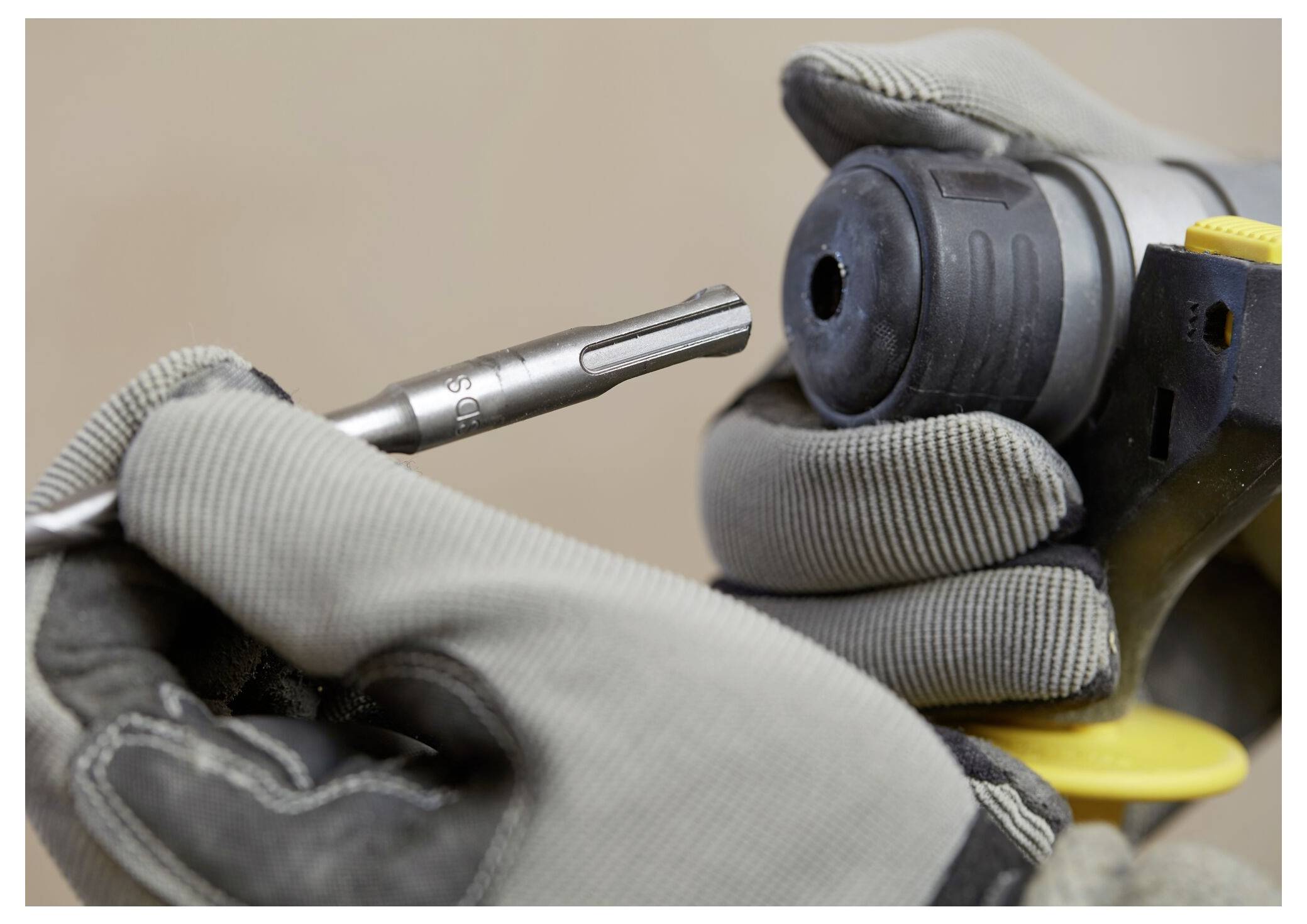 Nahaufnahme von behandschuhten Händen, die einen Bohrer in eine Elektrobohrmaschine einführen, um ordnungsgemäße Werkzeughandhabung und Sicherheitsvorkehrungen zu demonstrieren.