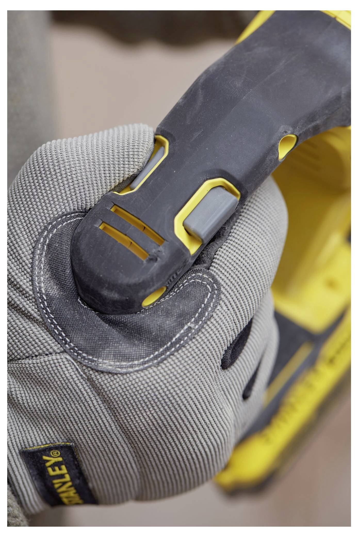 Eine Person, die graue Handschuhe trägt, hält ein gelb-schwarzes Elektrowerkzeug und konzentriert sich dabei auf den Griff und die Griffmulde.