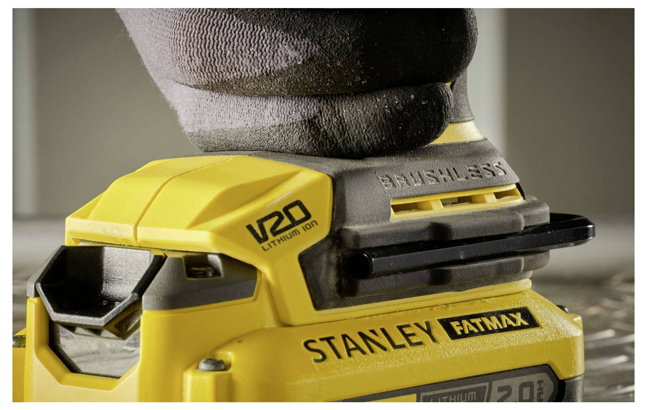 Eine behandschuhte Hand bedient ein gelbes kabelloses Stanley-Werkzeug mit bürstenlosen Motoren auf einer Oberfläche. Das Werkzeug trägt die Kennzeichnung „V20 Lithium Ion