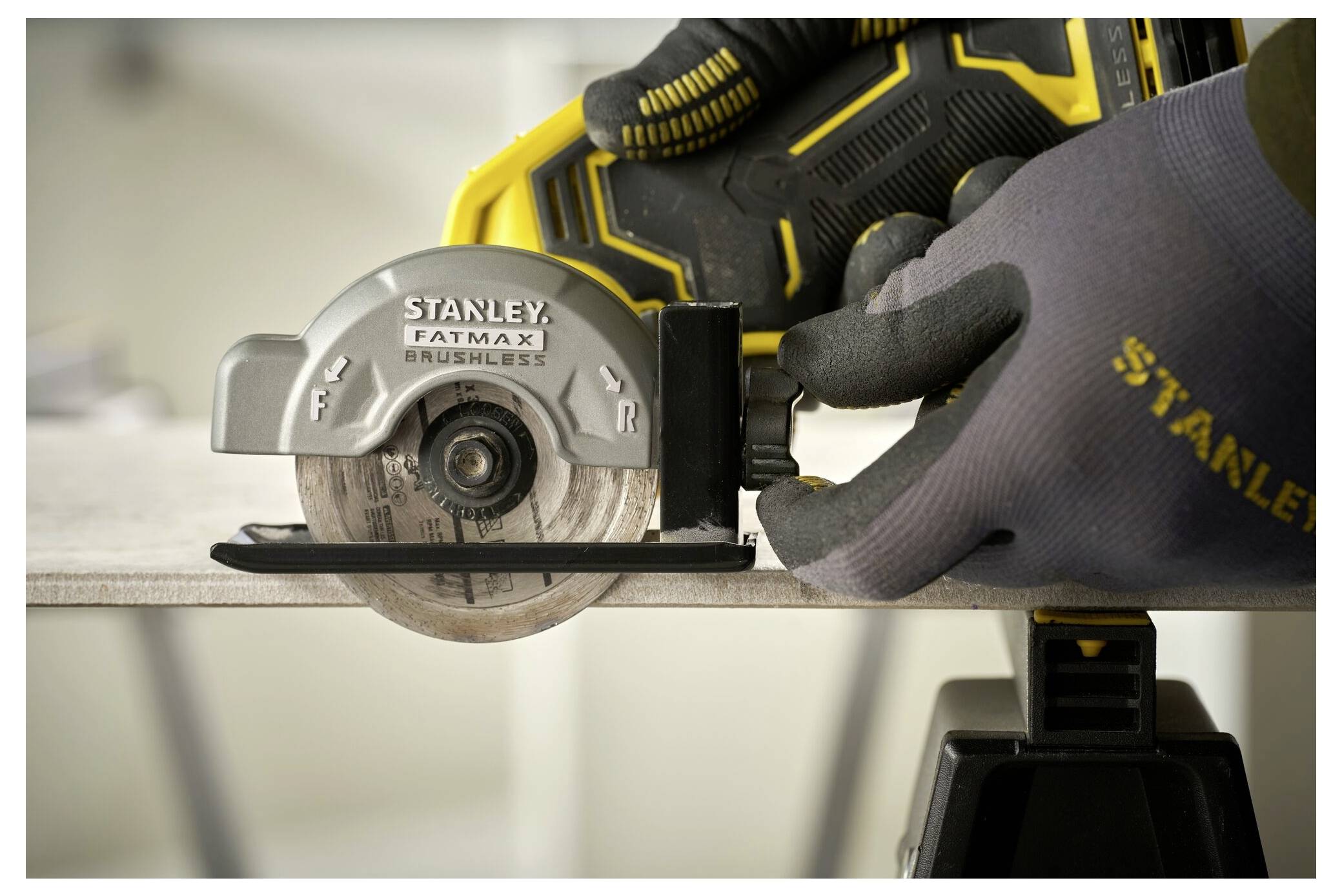 Eine Person, die Handschuhe und Stiefel trägt, benutzt einen gelben Bohrer auf einer dunklen Steinplatte, die auf Holzpaletten platziert ist. Staub ist sichtbar.