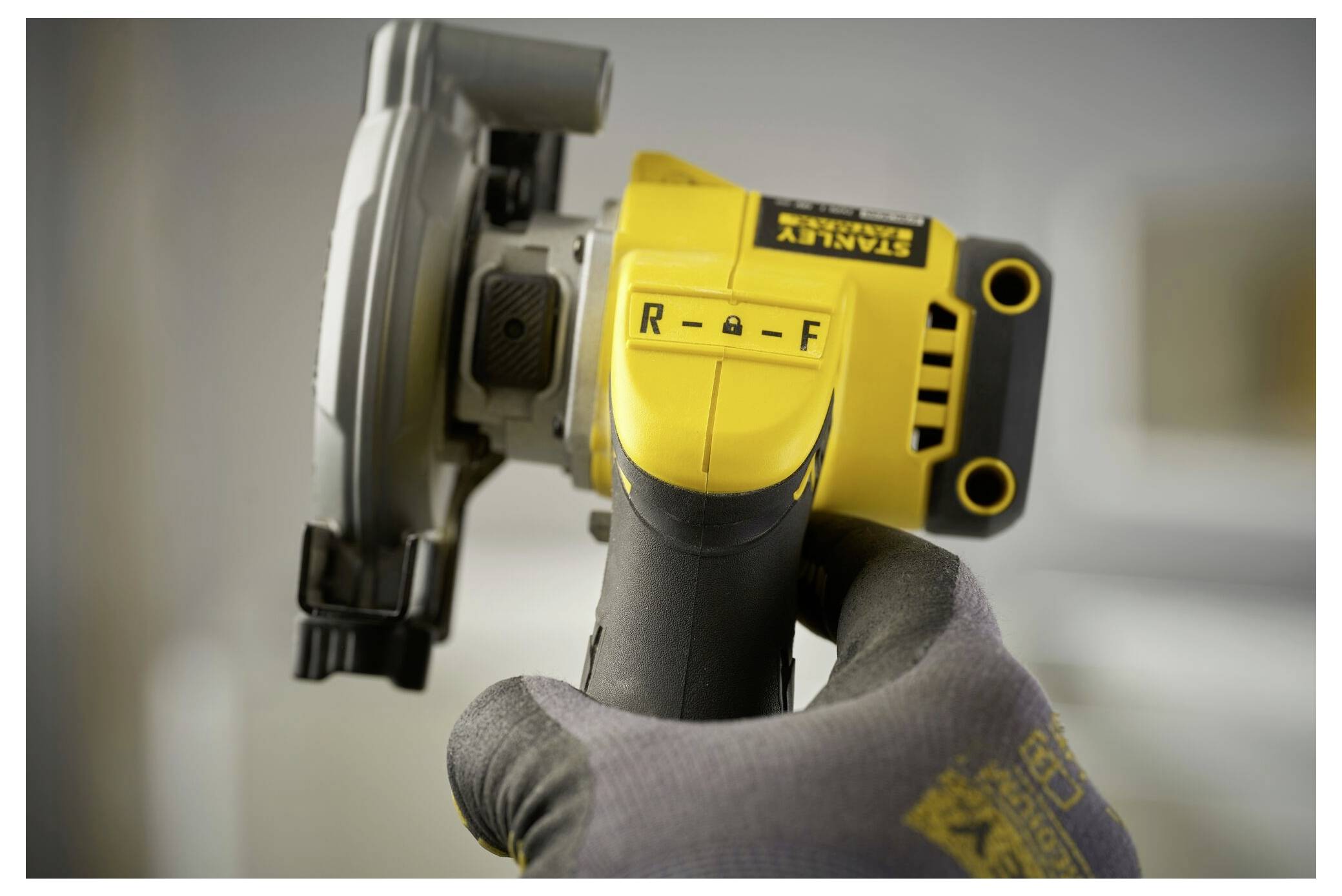 Eine behandschuhte Hand hält ein Stanley-Elektrowerkzeug mit gelbem und grauem Gehäuse und konzentriert sich auf einen Schalter mit den Beschriftungen „R