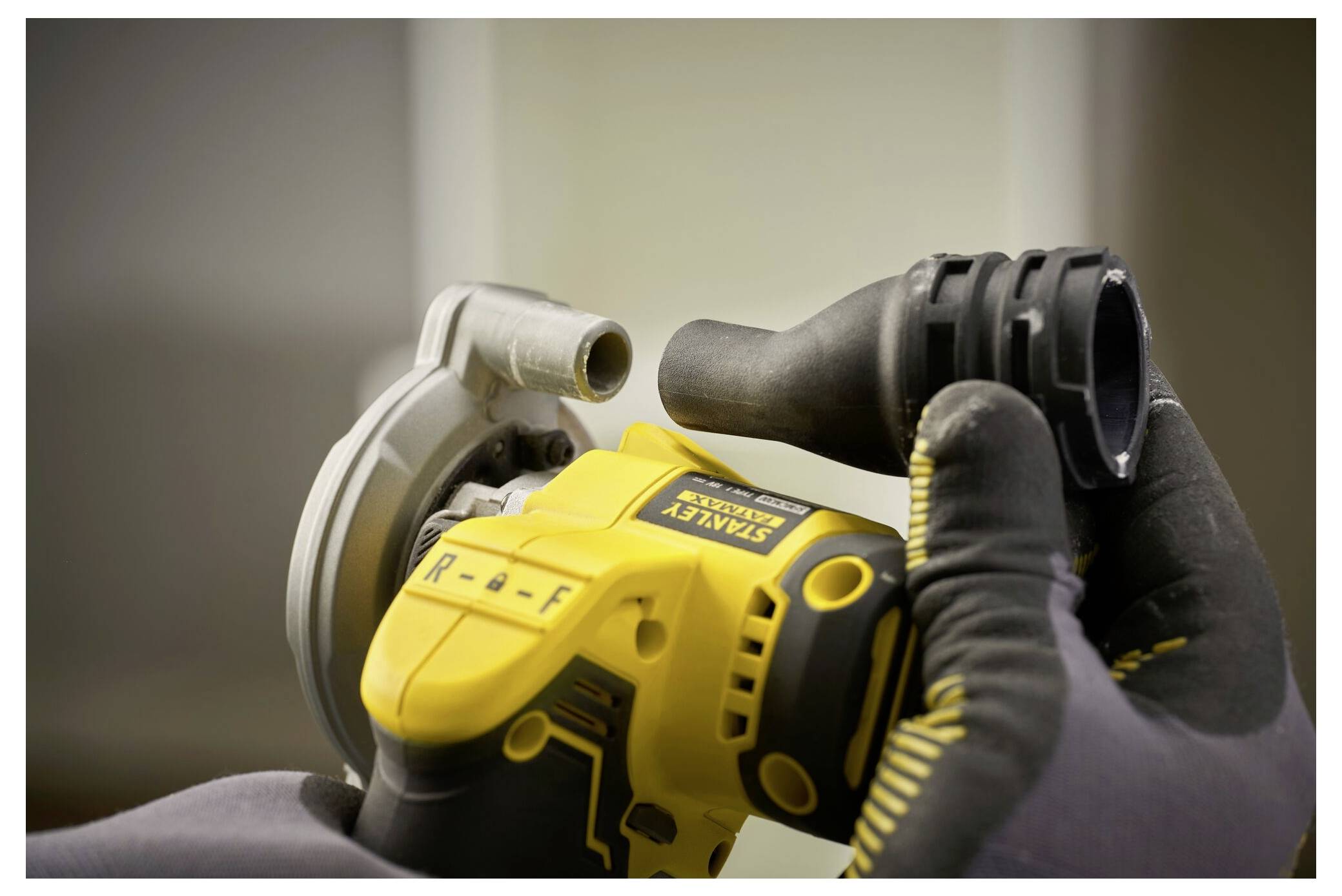 Eine Person trägt Handschuhe und hält ein gelbes Stanley-Elektrowerkzeug.
