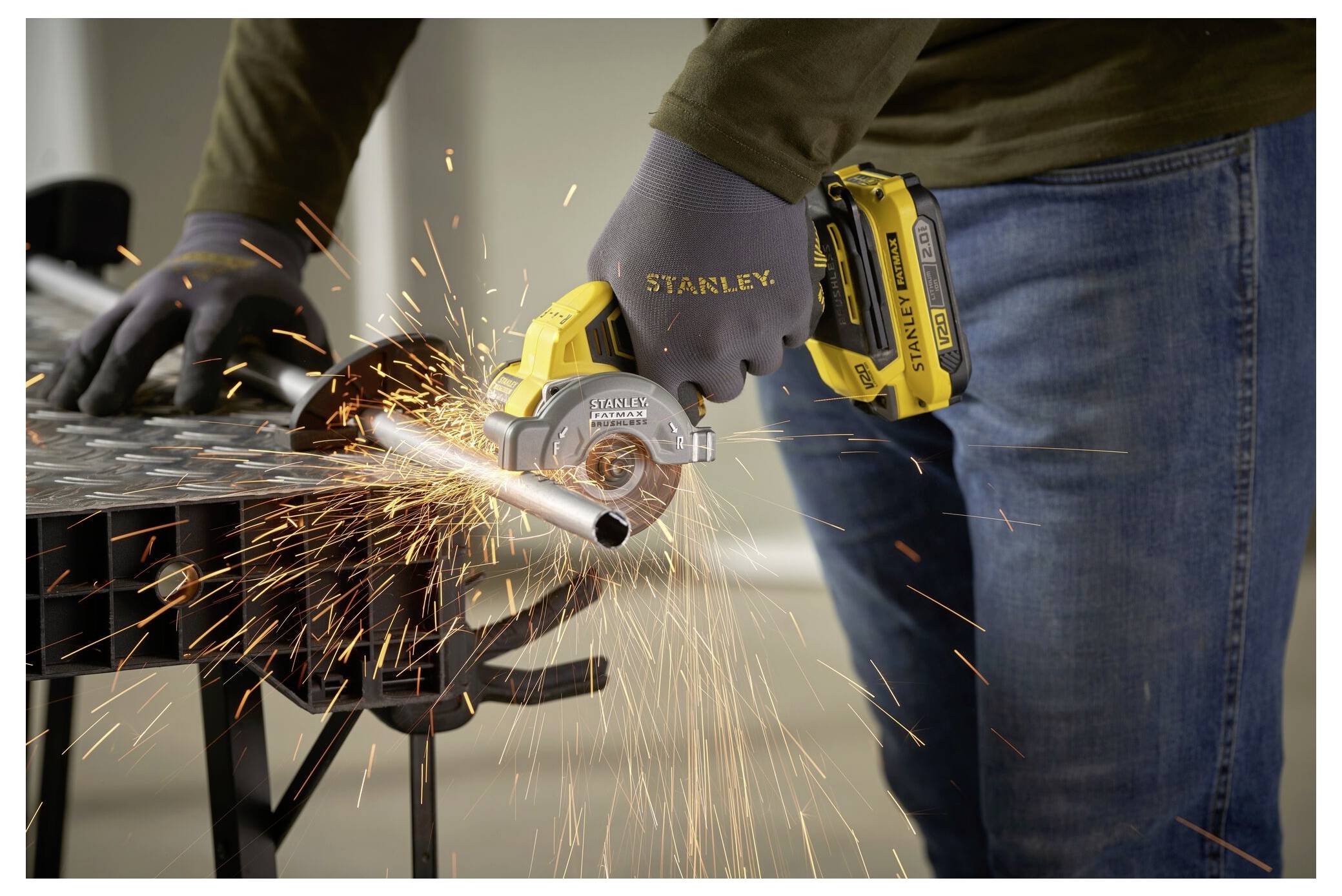 Eine Person in Handschuhen benutzt ein Elektrowerkzeug, um ein Metallrohr zu schneiden, wobei Funken fliegen. Das Werkzeug ist batteriebetrieben und trägt die Marke „Stanley
