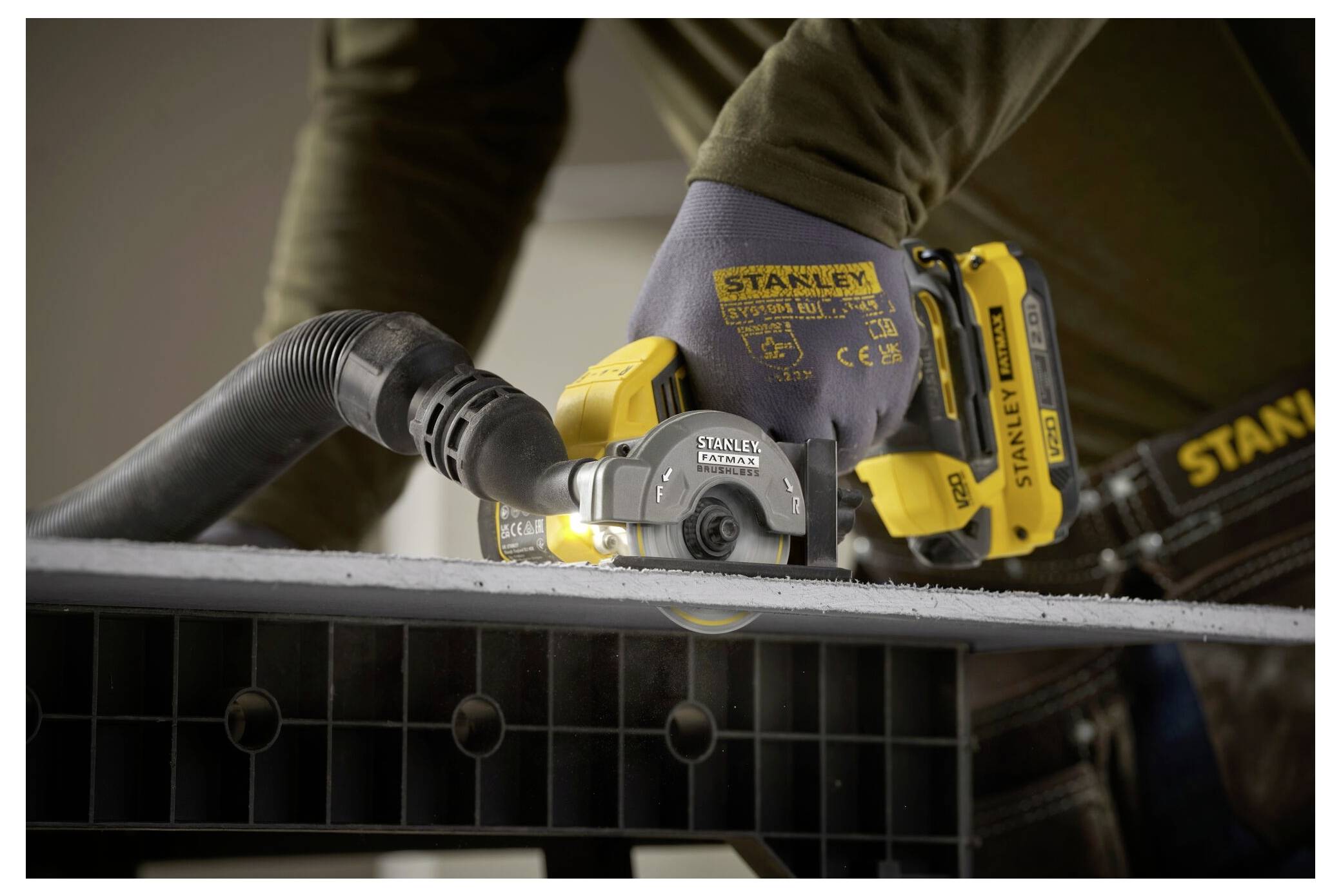 Eine Person, die Handschuhe trägt, benutzt ein Stanley Elektrowerkzeug zum Schneiden eines Bretts, mit Fokus auf das Werkzeug und dessen Verwendung zum präzisen Schneiden.