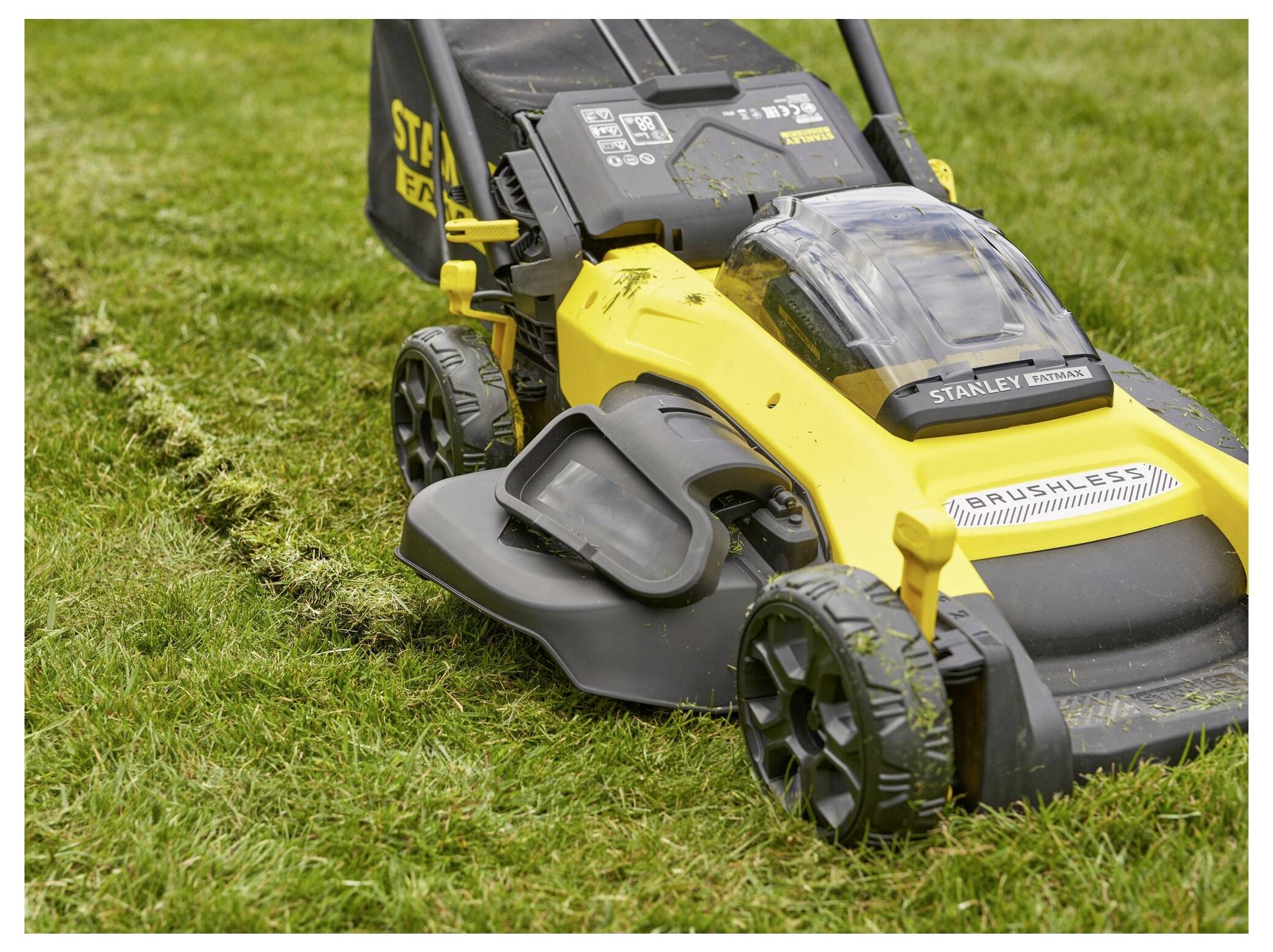 Ein gelber Rasenmäher mit großen Rädern schneidet Gras. Das Seitenfach des Mähers ist offen und hinterlässt einen gemähten Weg im Gras.