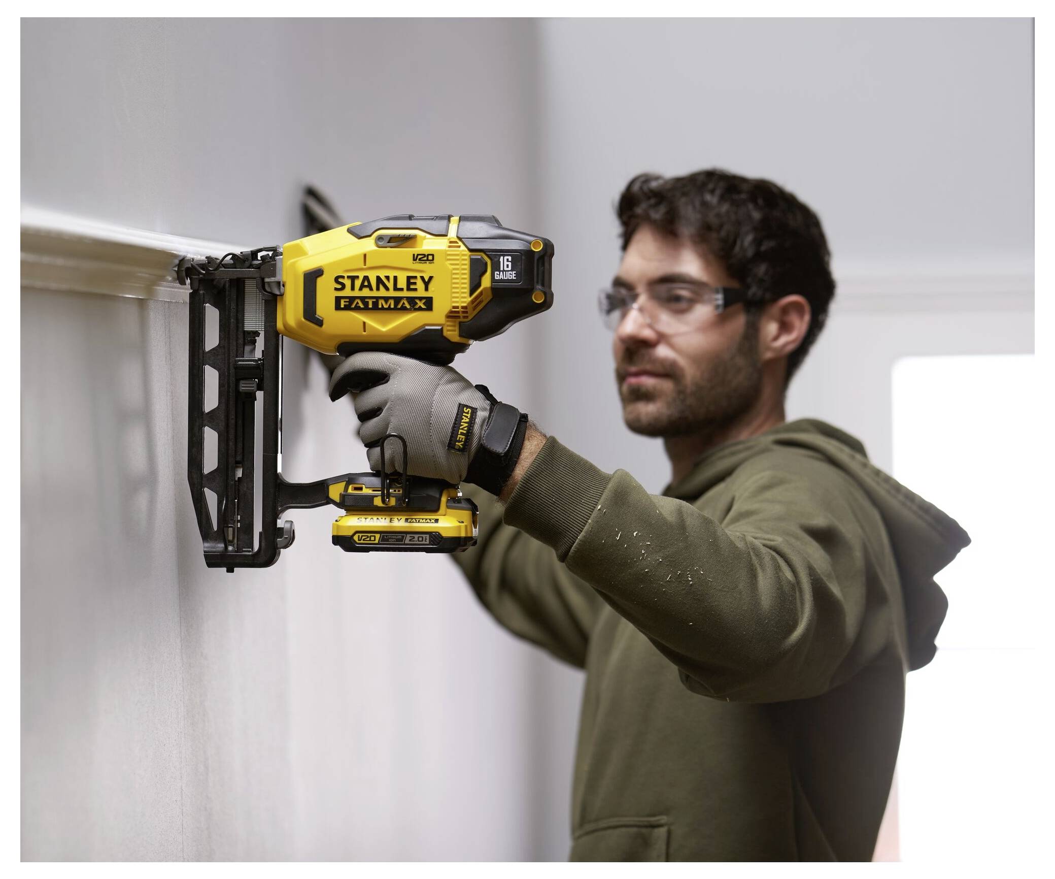 Eine Person trägt Schutzbrille und verwendet eine gelbe Stanley FatMax Nagelmaschine, um Zierleisten an einer Wand zu befestigen.