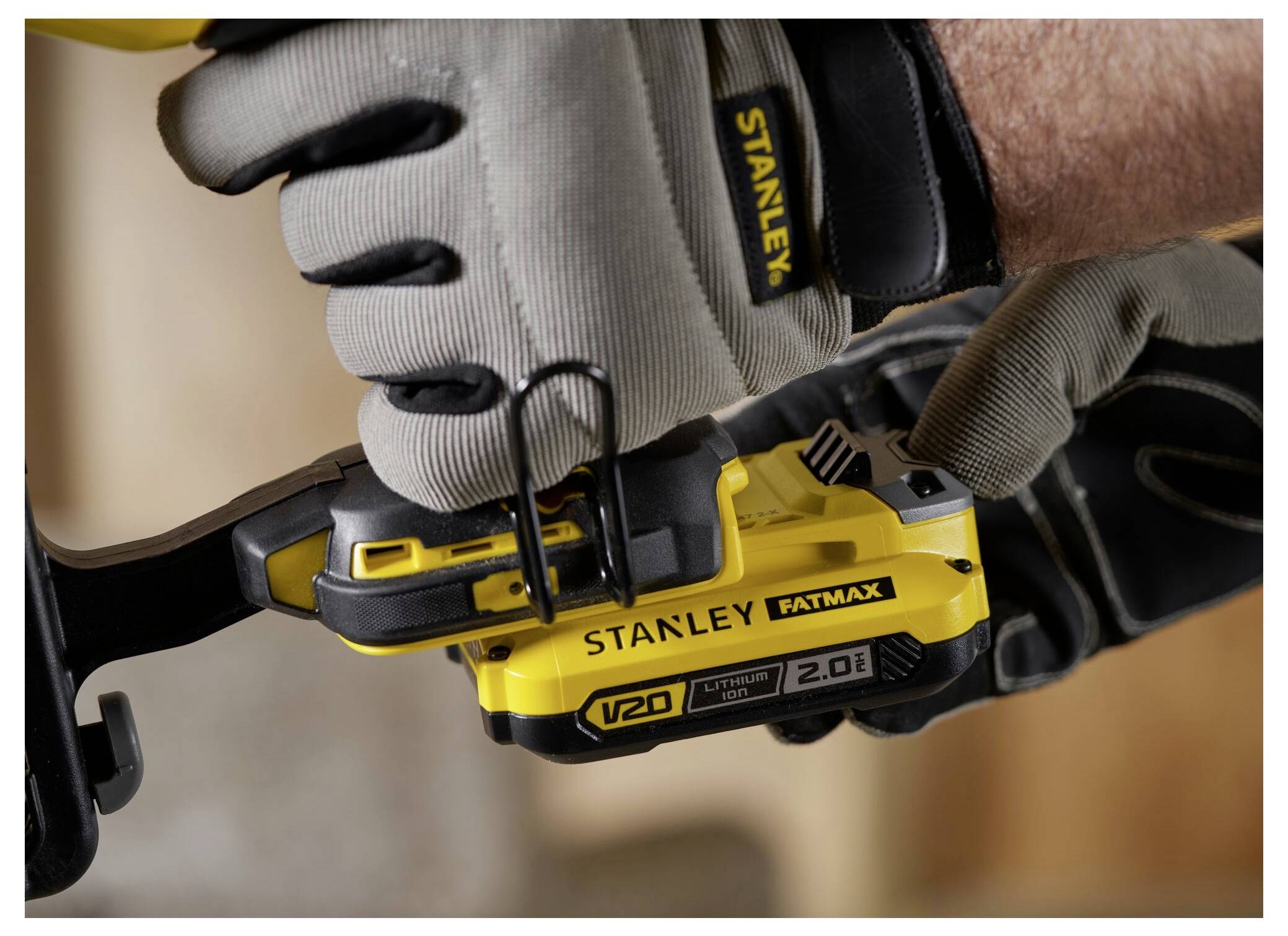 Eine behandschuhte Hand bedient ein gelbes Stanley Fatmax V20 Elektrowerkzeug, was auf den Einsatz im Bauwesen oder bei Reparaturarbeiten hindeutet.