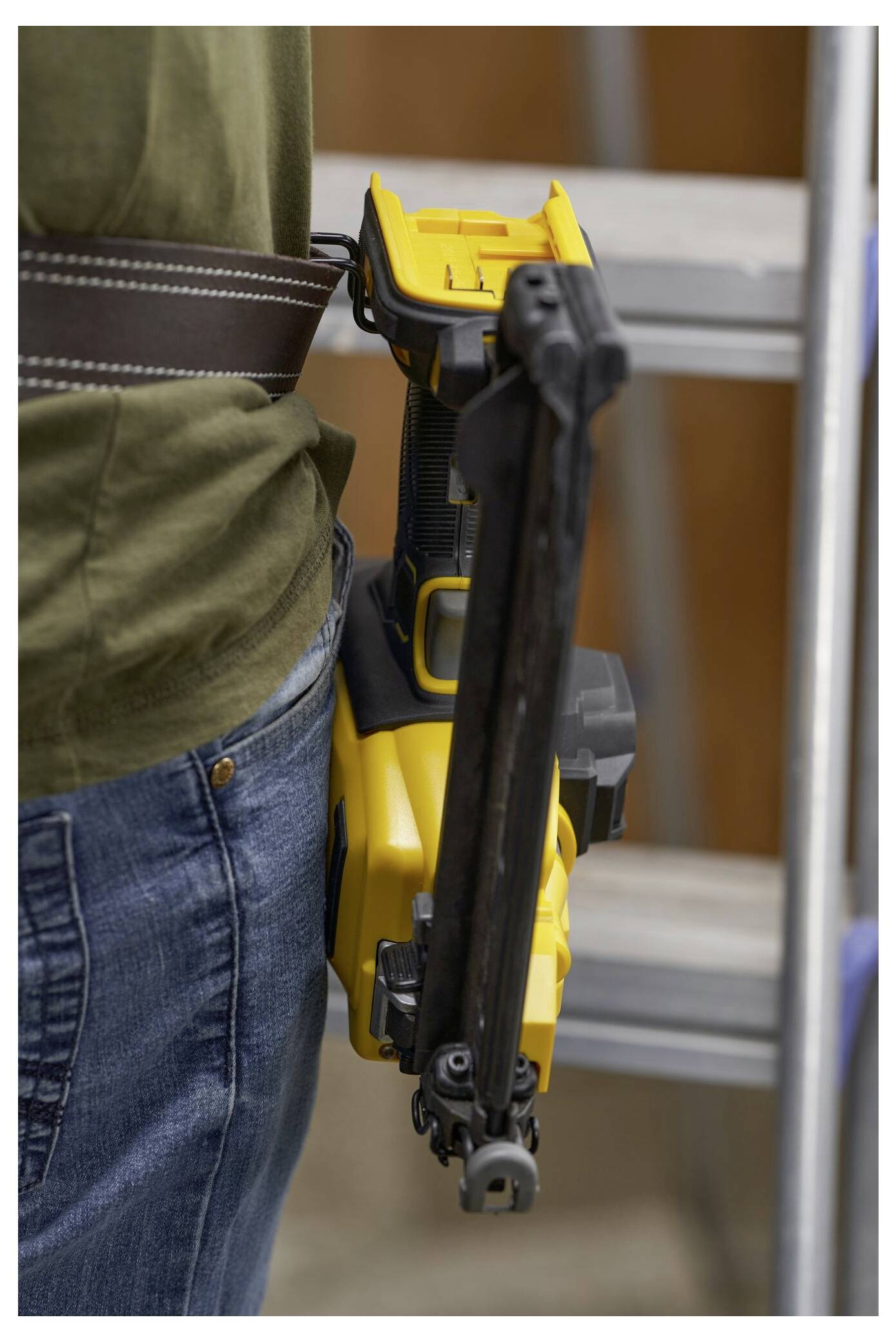 Eine Person, die neben einer Leiter steht, trägt eine gelbe Nagelmaschine, die an ihrem Gürtel befestigt ist.