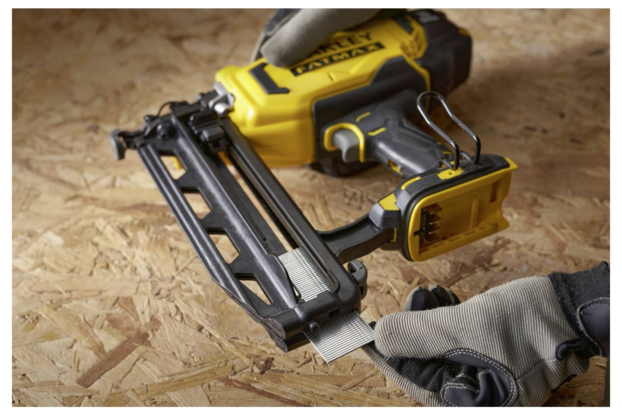 Eine Person mit Handschuhen lädt Nägel in eine gelbe Nagelspistole, die auf einer Holzoberfläche ruht.