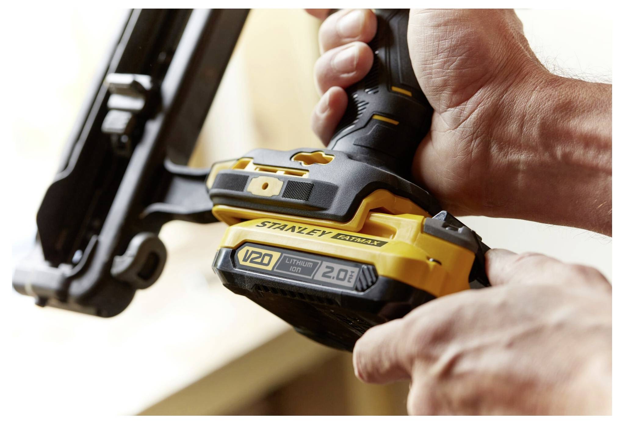 Eine Person befestigt eine 20V-Lithium-Batterie an einem Stanley Fatmax-Werkzeug und konzentriert sich dabei auf den Griff und die Batteriemerkmale in einer Werkstattsituation.